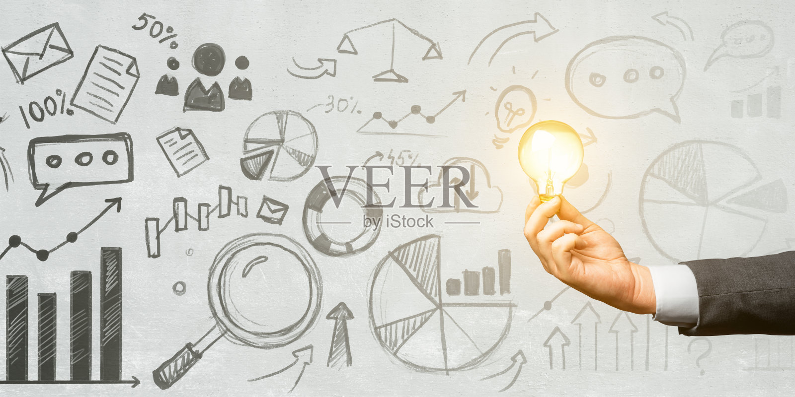 手持明亮的灯泡与商业涂鸦在灰色背景。照片摄影图片