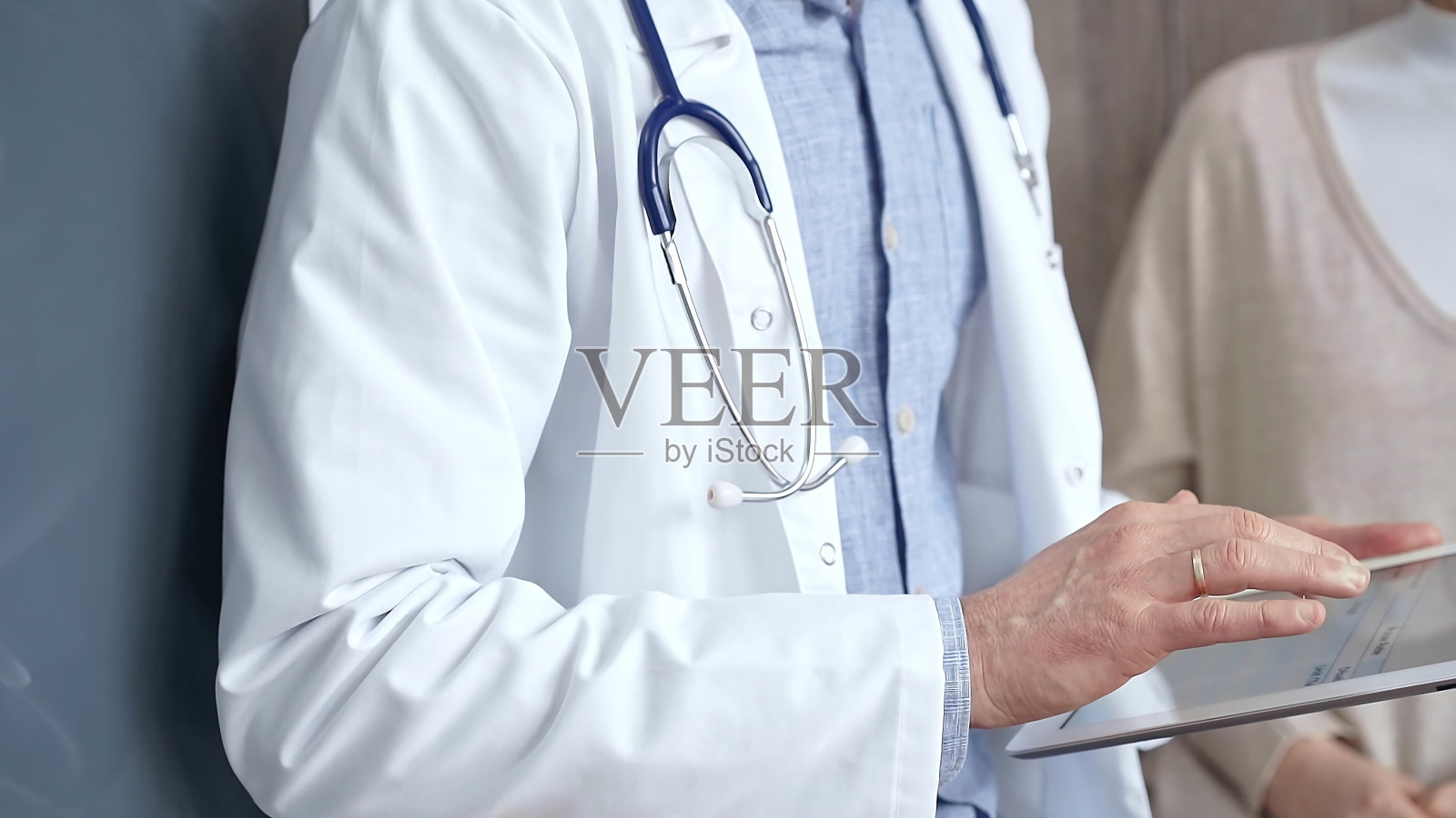 医生和病人。一个医生的手在写字板上做笔记的特写，背景是一个女人。医药和保健照片摄影图片