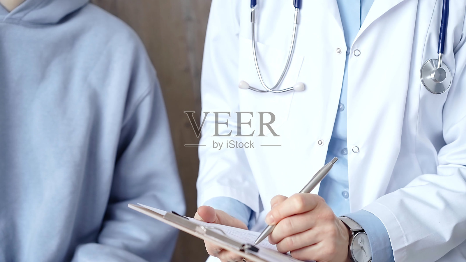 医生一边在剪贴板上做医疗笔记，一边用剪贴板咨询病人。医学的概念照片摄影图片