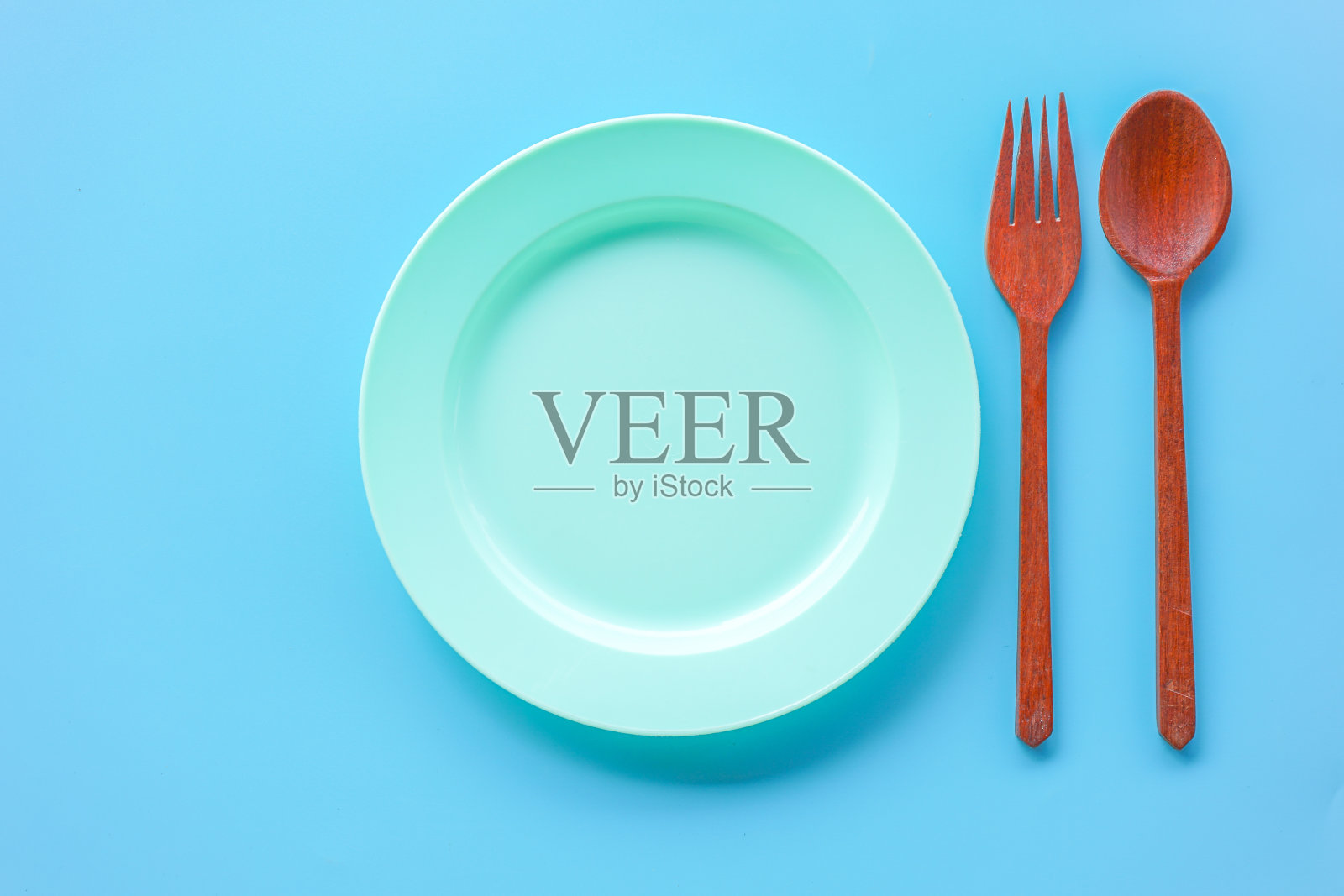 蓝色背景上的木质勺子和叉子的空绿色塑料盘子的平面视图照片摄影图片