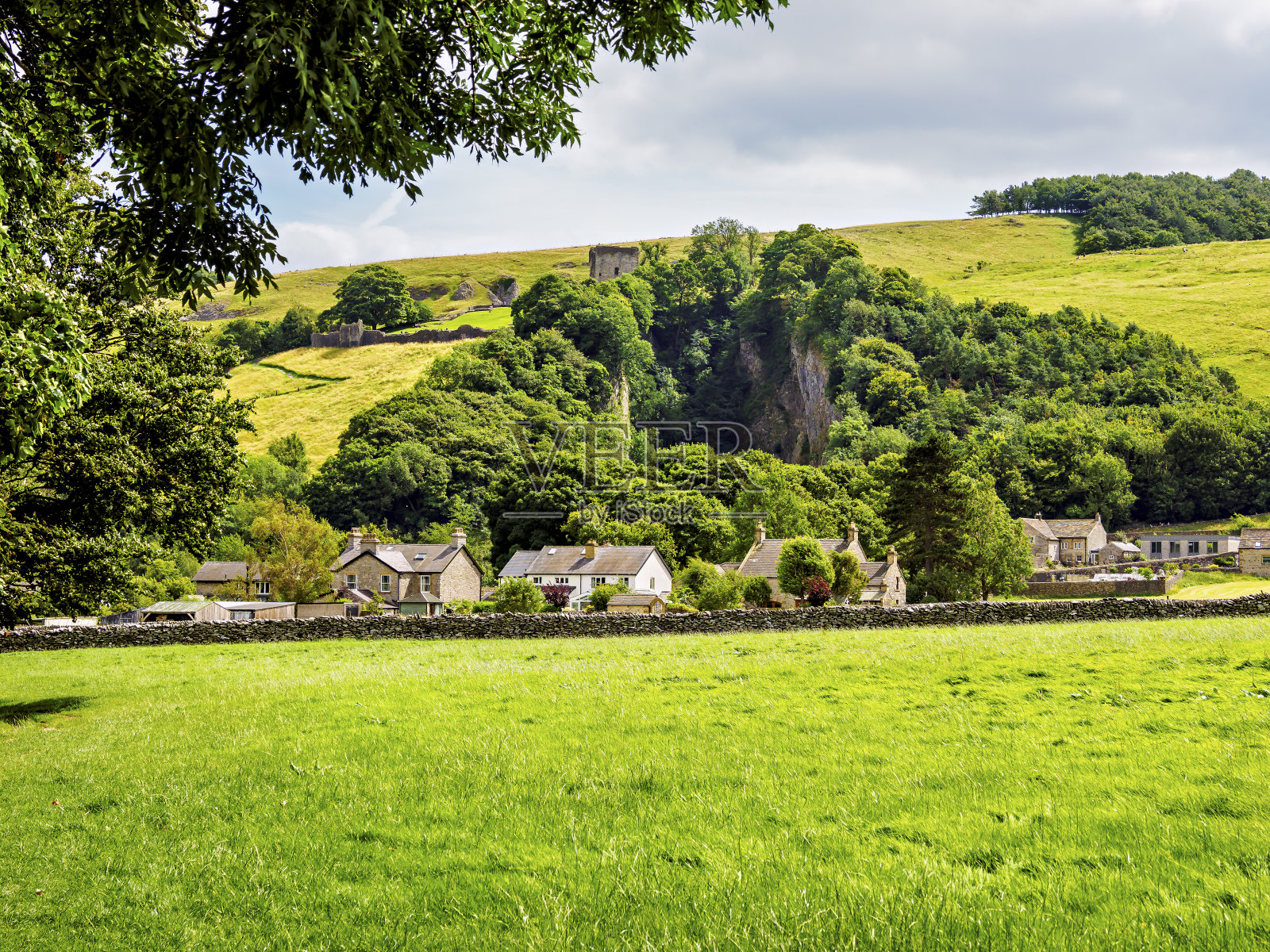 田园诗般的乡村坐落在郁郁葱葱的绿色山丘上，在多云的天空下，散发着宁静和自然之美。照片摄影图片