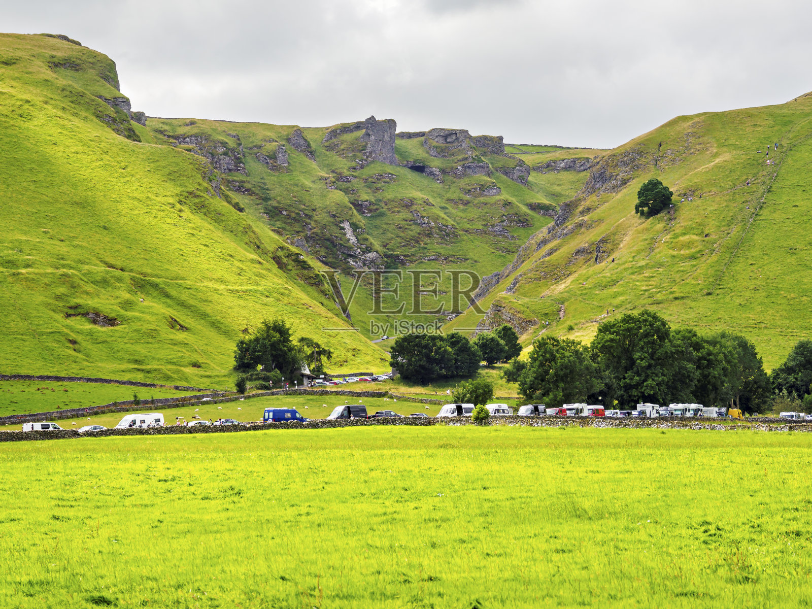 郁郁葱葱的绿色山谷的美景，在多云的日子里，露营车和汽车停在岩石山脚下。照片摄影图片