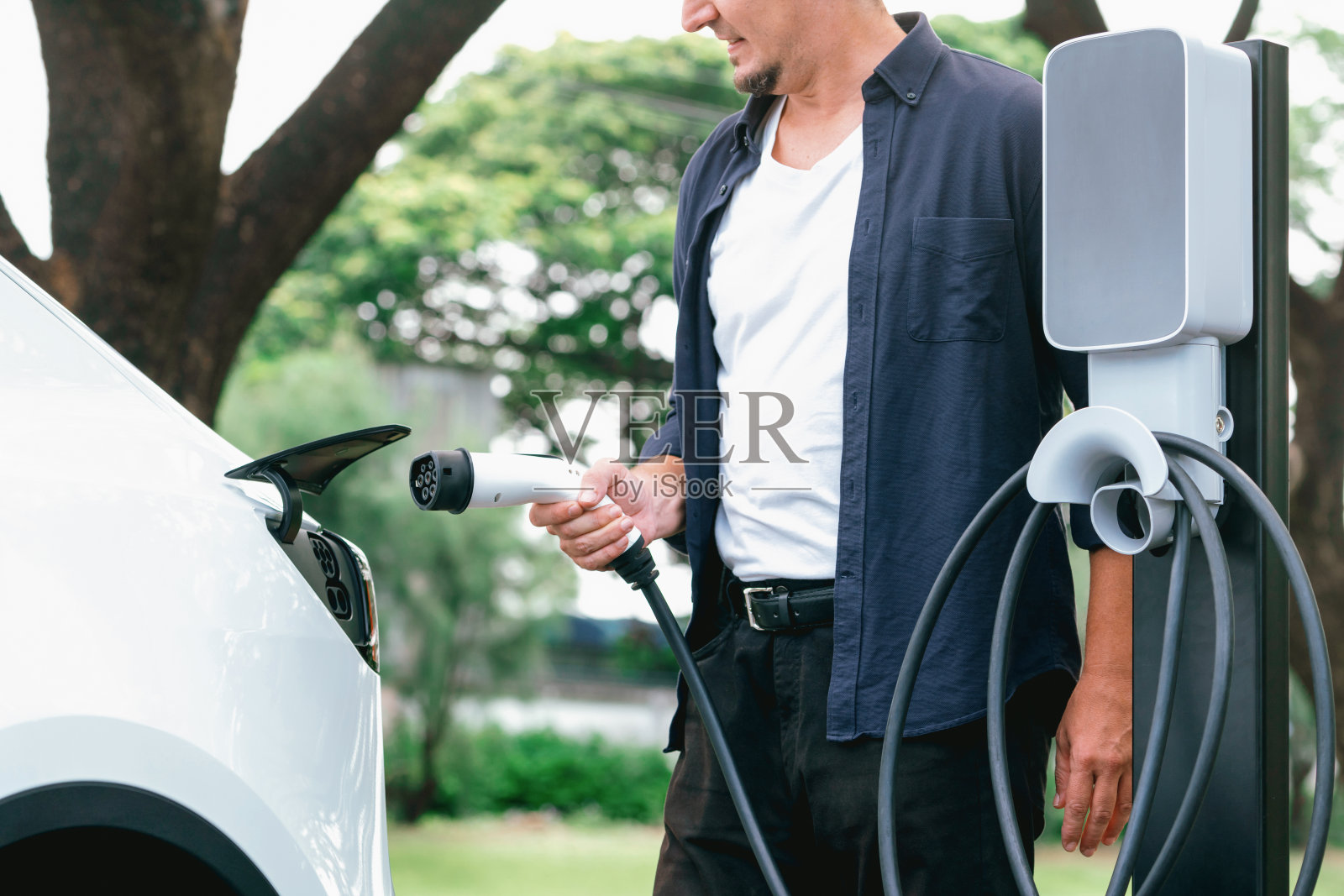 一名男子在旅途中给电动汽车充电。高举照片摄影图片