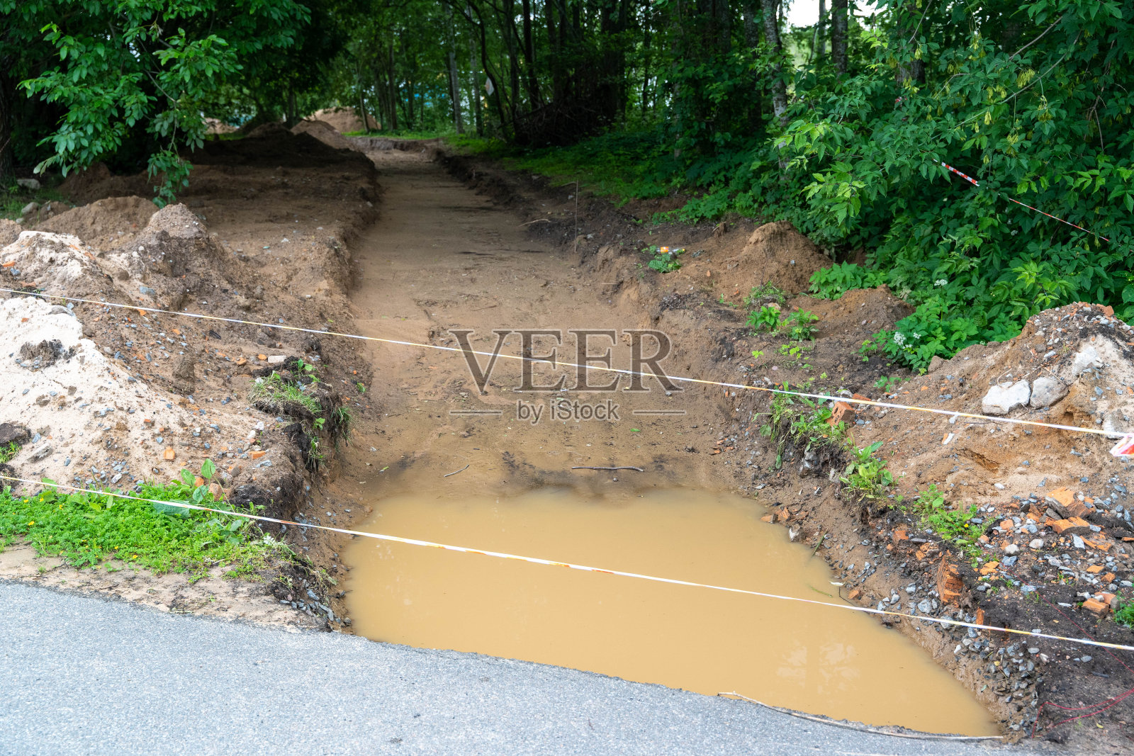 建筑工地与泥泞的水坑，土路，山，森林在右边照片摄影图片