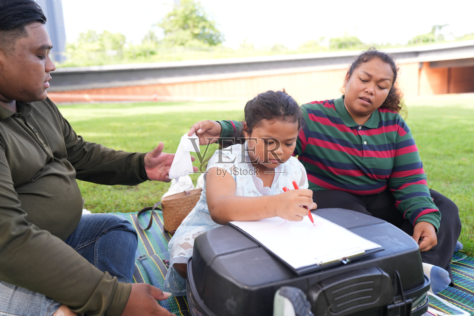 一个又大又胖的亚洲家庭，爸爸、妈妈、女儿在公园里野餐，他们坐着吃零食。他们坐着做作业，互相送花。他们很开心。照片摄影图片