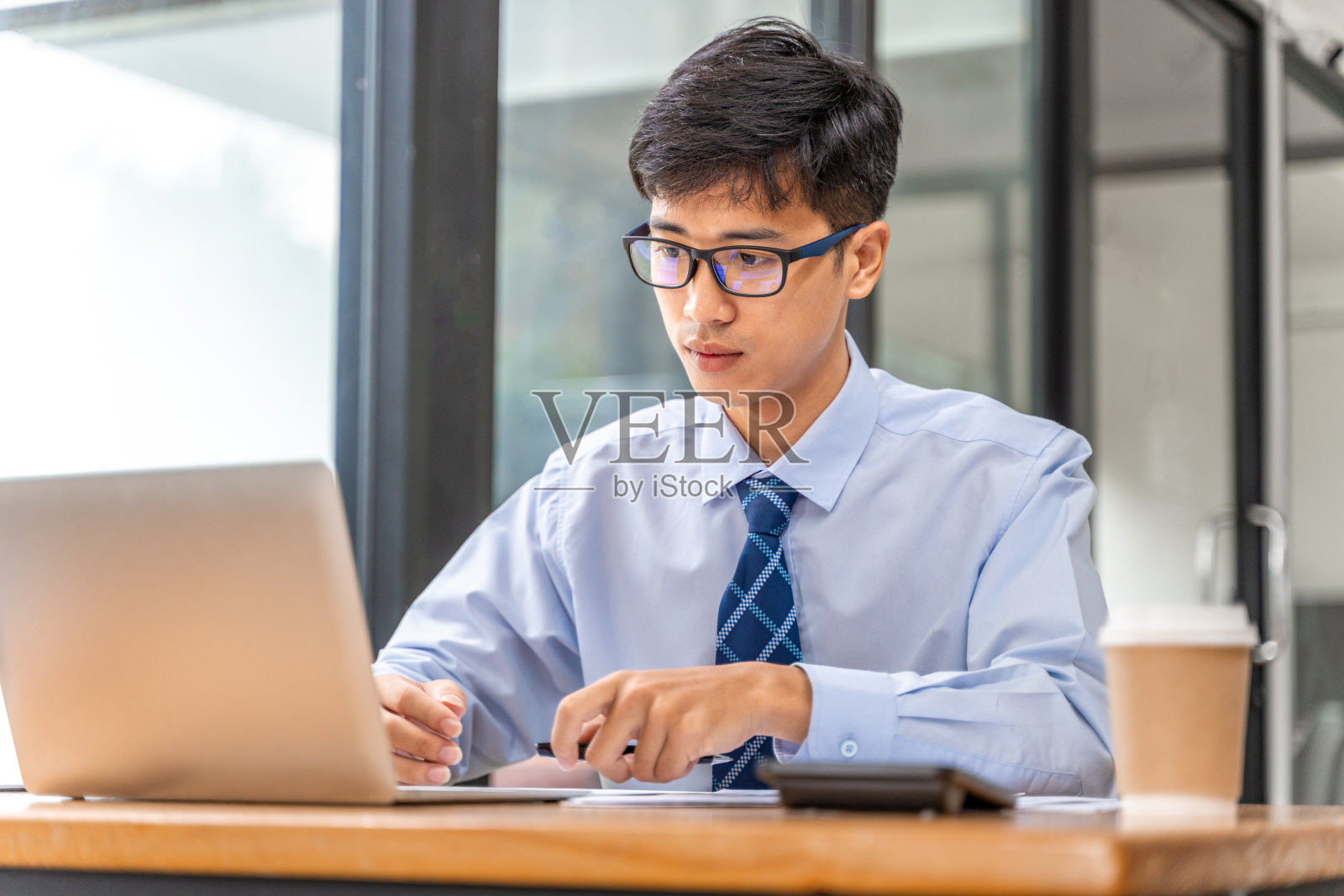 年轻的商人在他的办公室里做他的项目，从打印的表格和笔记本电脑中检查业务结果数据照片摄影图片