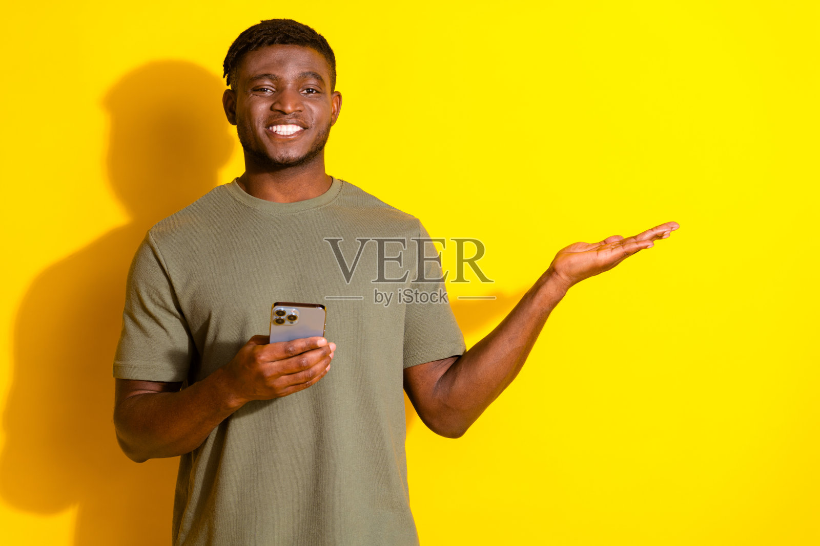 照片中，开朗有趣的好男人穿着卡其色时尚的衣服，拿着空荡荡的小玩意，孤立在黄色的背景上照片摄影图片