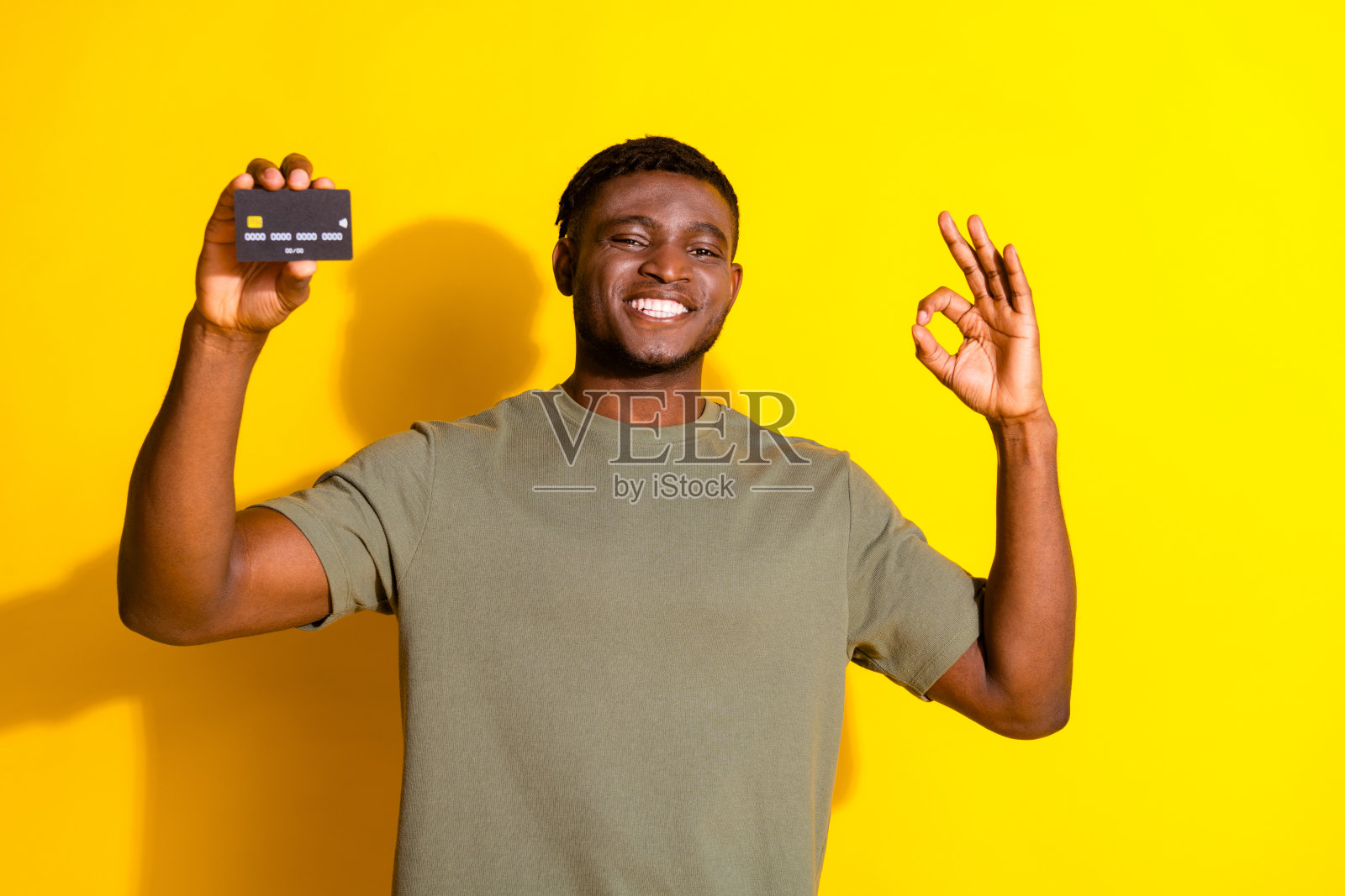 一个穿着时髦卡其布衣服的快乐满意的男人的照片。无现金的银行卡被隔离在黄色背景上照片摄影图片