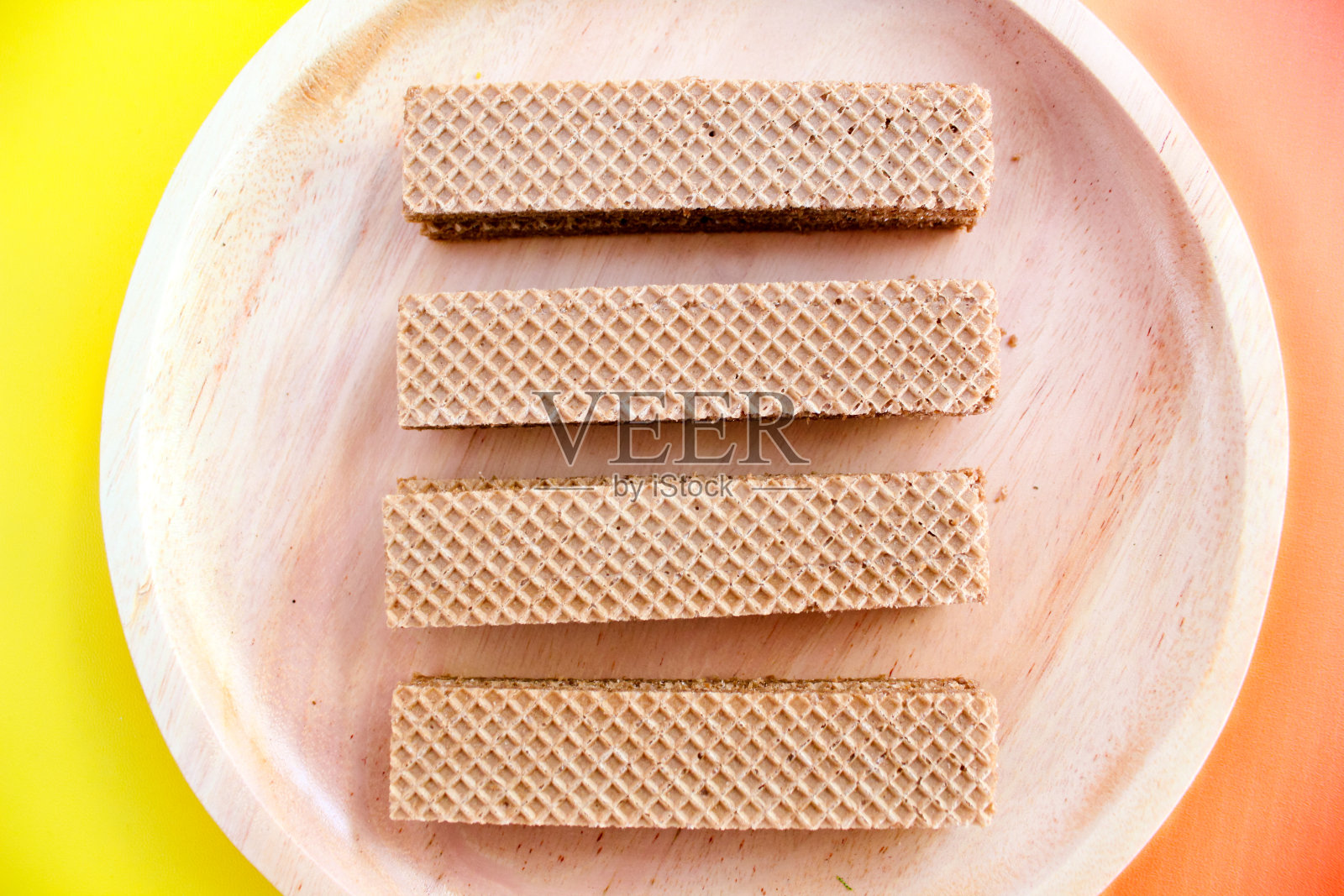 木制盘子上的巧克力华夫饼被隔离在橙色和黄色的背景上。脆脆的点心甜点。美食摄影概念照片摄影图片