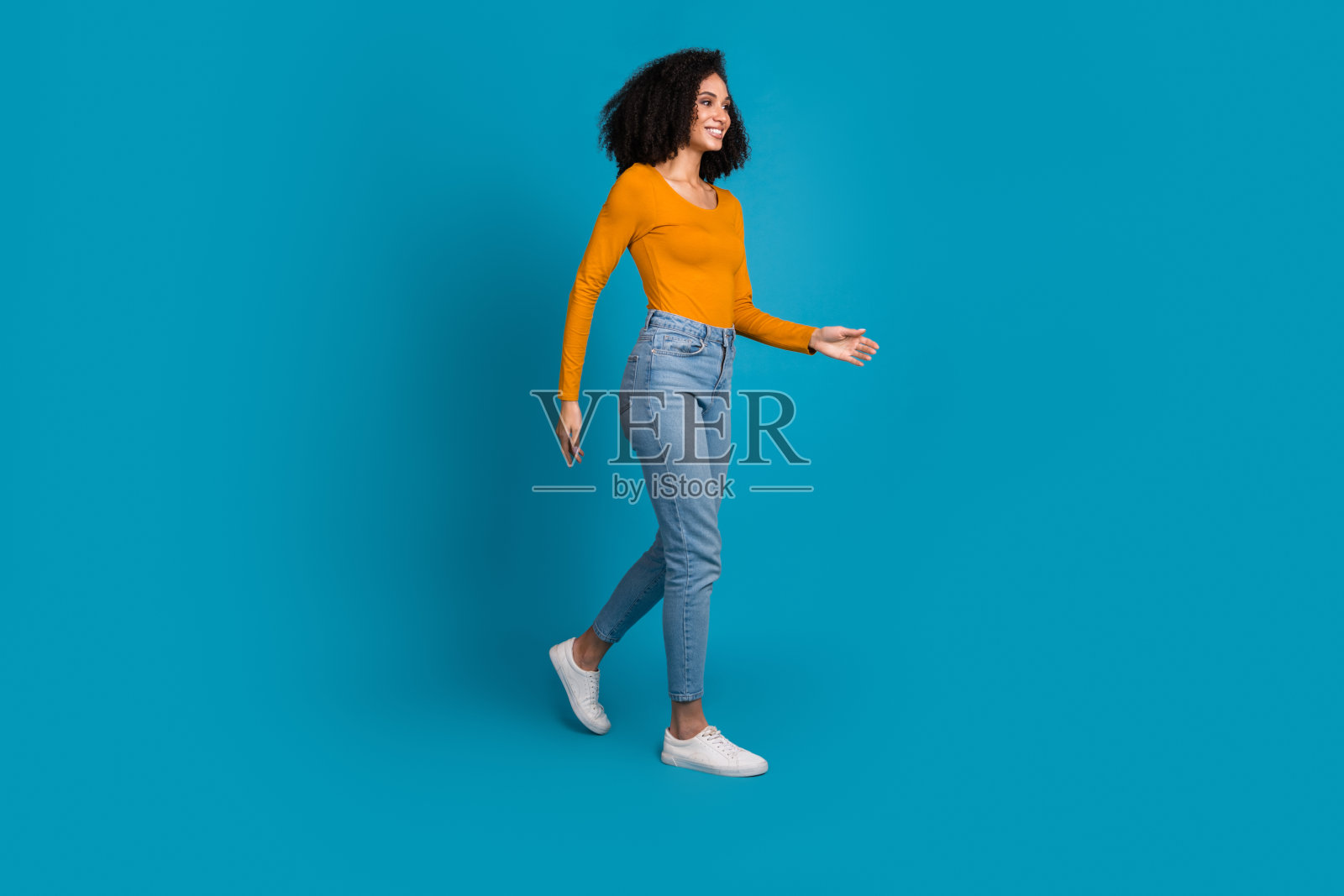 迷人的年轻女子穿着时尚的黄色衣服在蓝色背景上行走的全身照片照片摄影图片