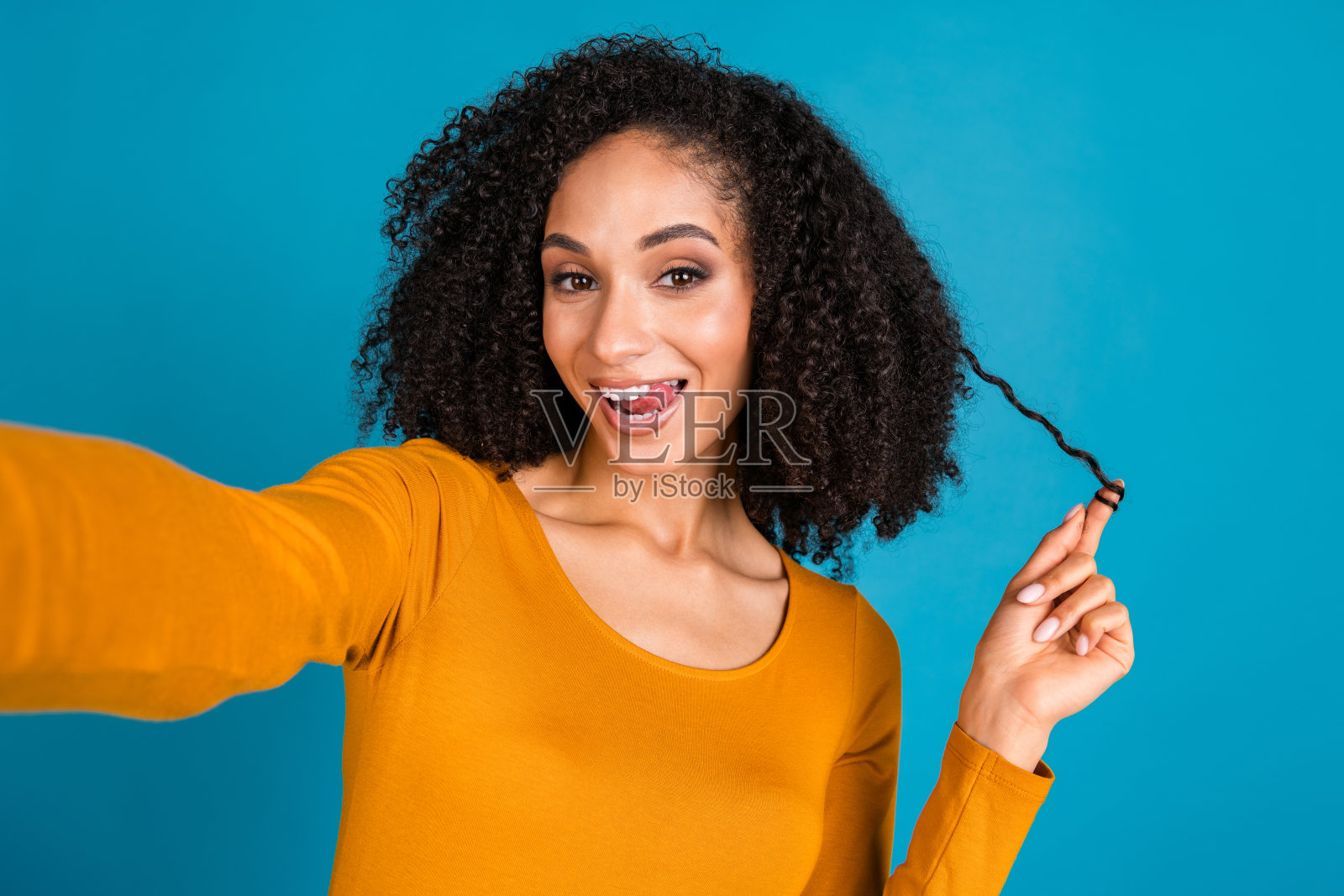 迷人的年轻女子手持发丝，穿着时尚的黄色衣服，在蓝色背景上自拍照片摄影图片