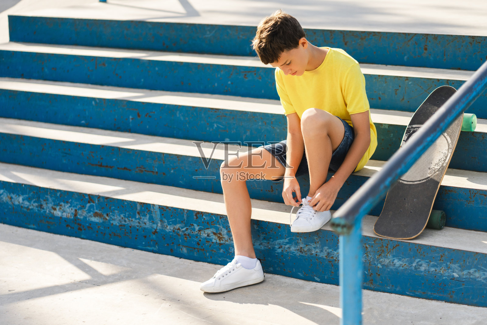 十几岁的滑冰男孩坐在楼梯上休息，系鞋带照片摄影图片