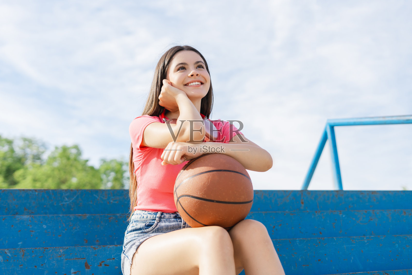 年轻微笑的孩子女孩拿着球，打篮球，坐在夏天的体育场照片摄影图片