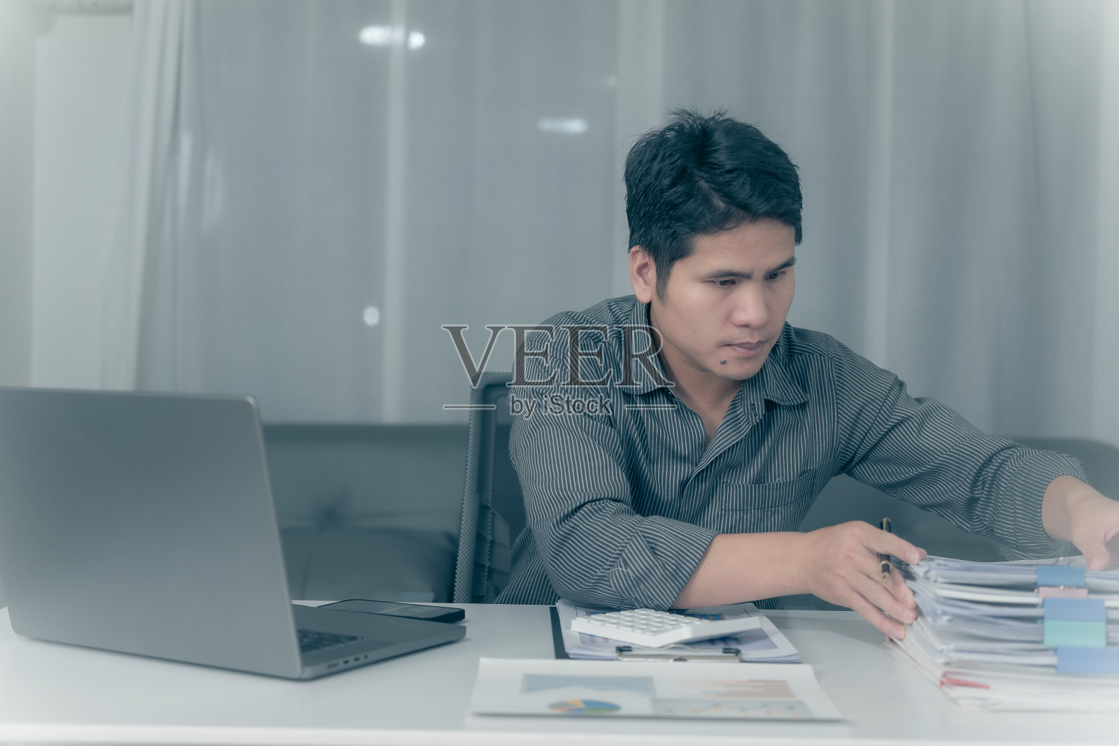 亚洲商人加班分析财务，制定预算。晚上在办公室用计算器计算照片摄影图片