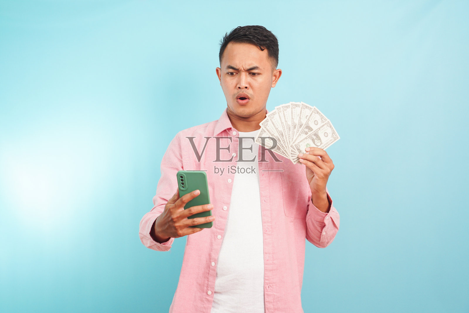 惊讶的表情男子看着手机，手里拿着站在蓝色背景上的美元照片摄影图片