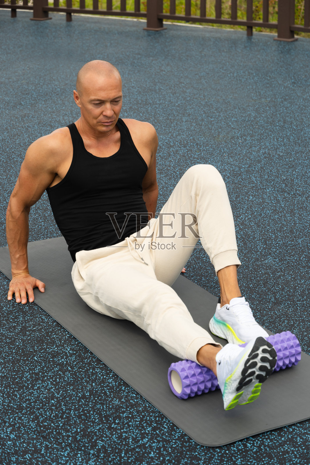 运动员在运动场的泡沫滚筒上伸展双腿。户外。早晨例行公事。照片摄影图片