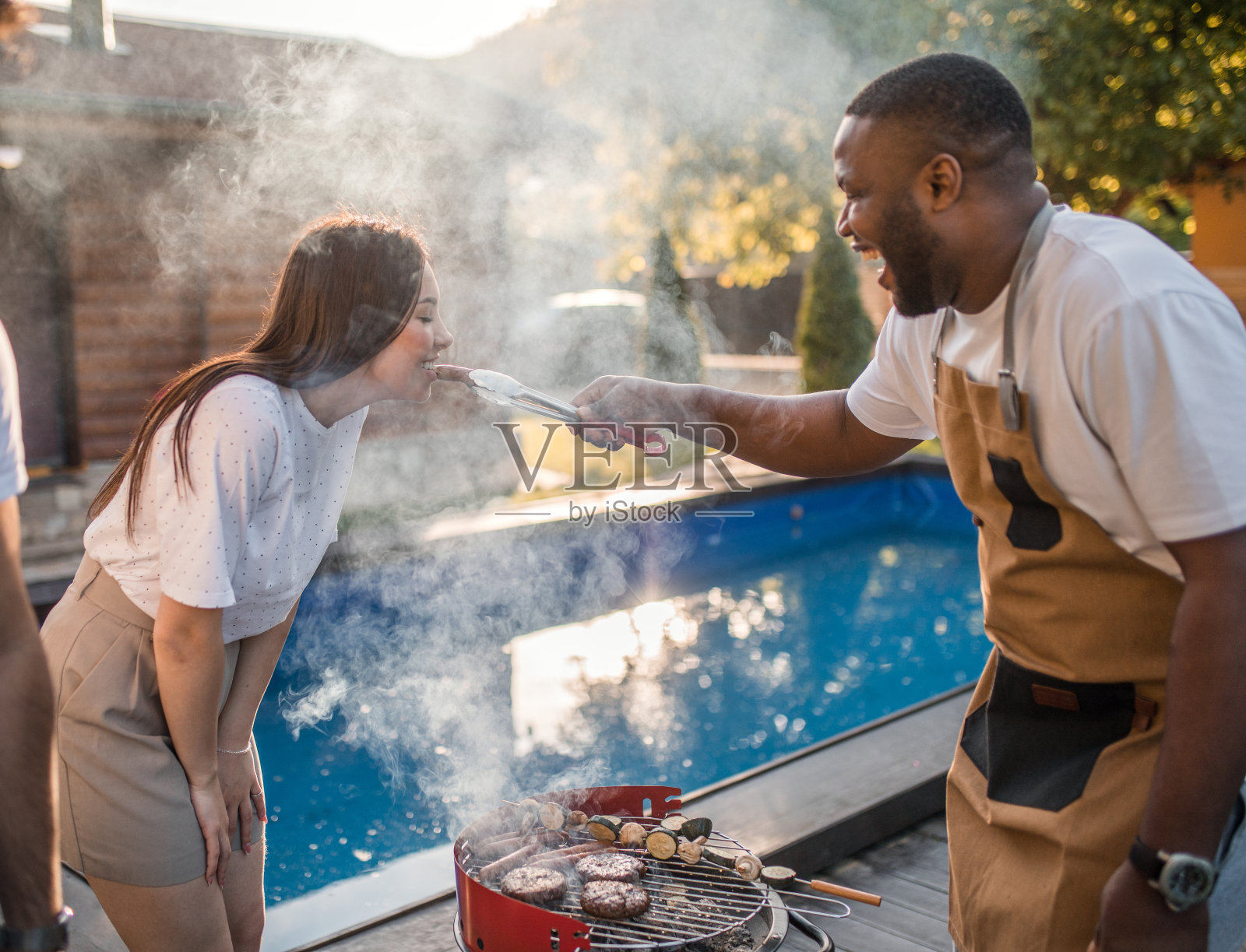 一个快乐的黑人给他的女性朋友品尝他正在烧烤的香肠照片摄影图片