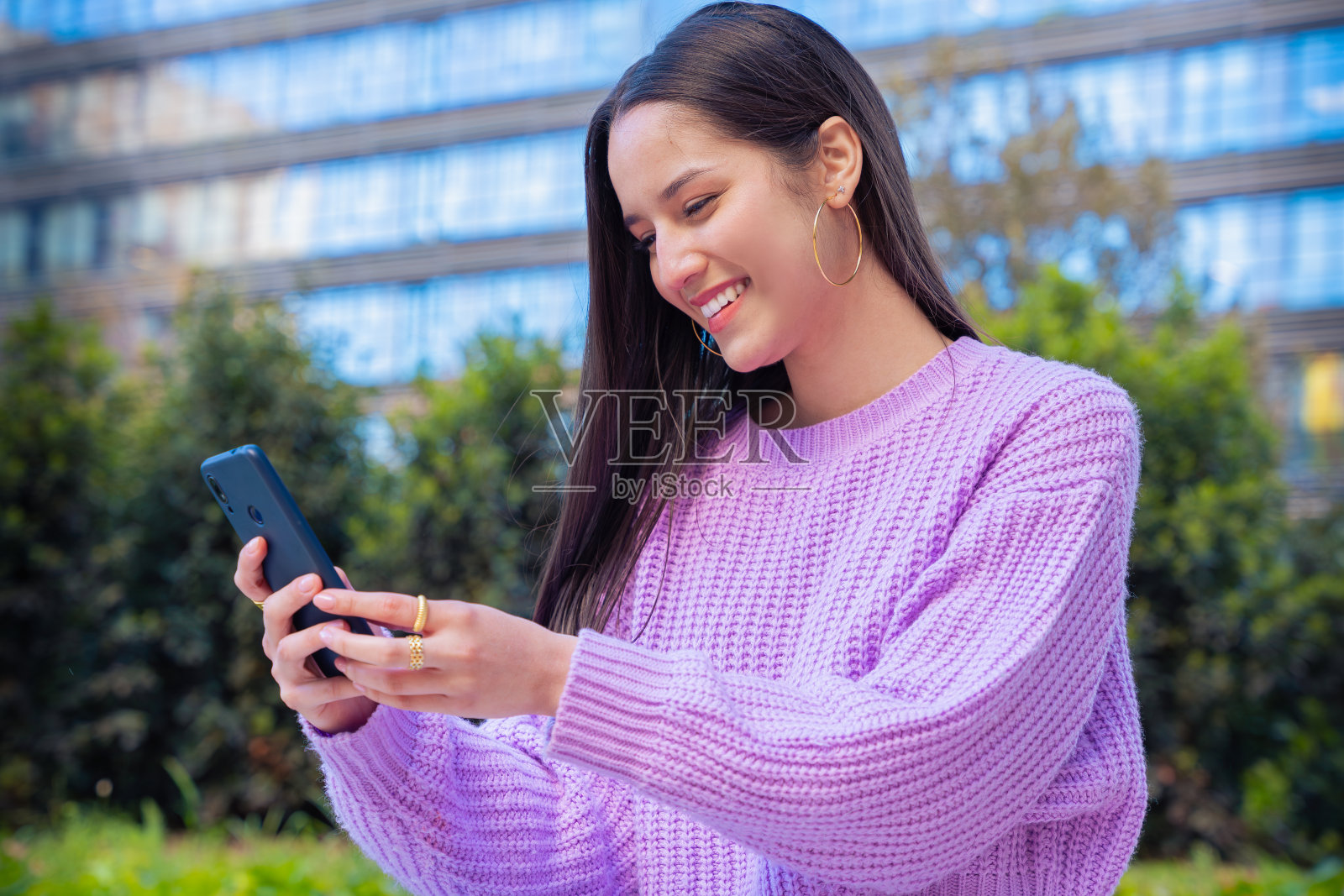 侧视图微笑的年轻女性在户外使用智能手机应用程序。照片摄影图片