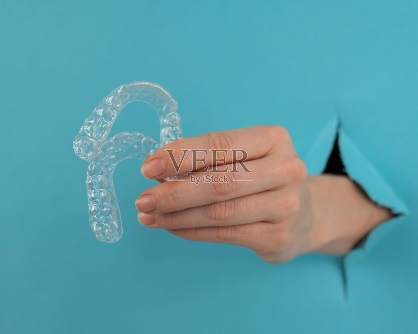 一只女性的手从蓝色背景的洞里伸出来，拿着可拆卸的护套。照片摄影图片