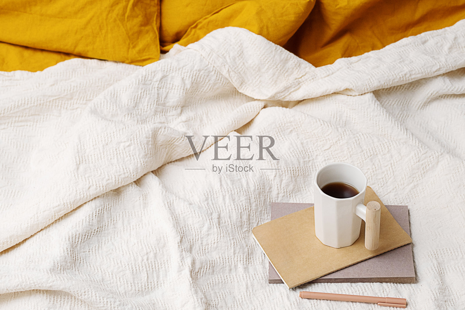 舒适的床，黄色的枕头，笔记本，笔和咖啡杯。照片摄影图片