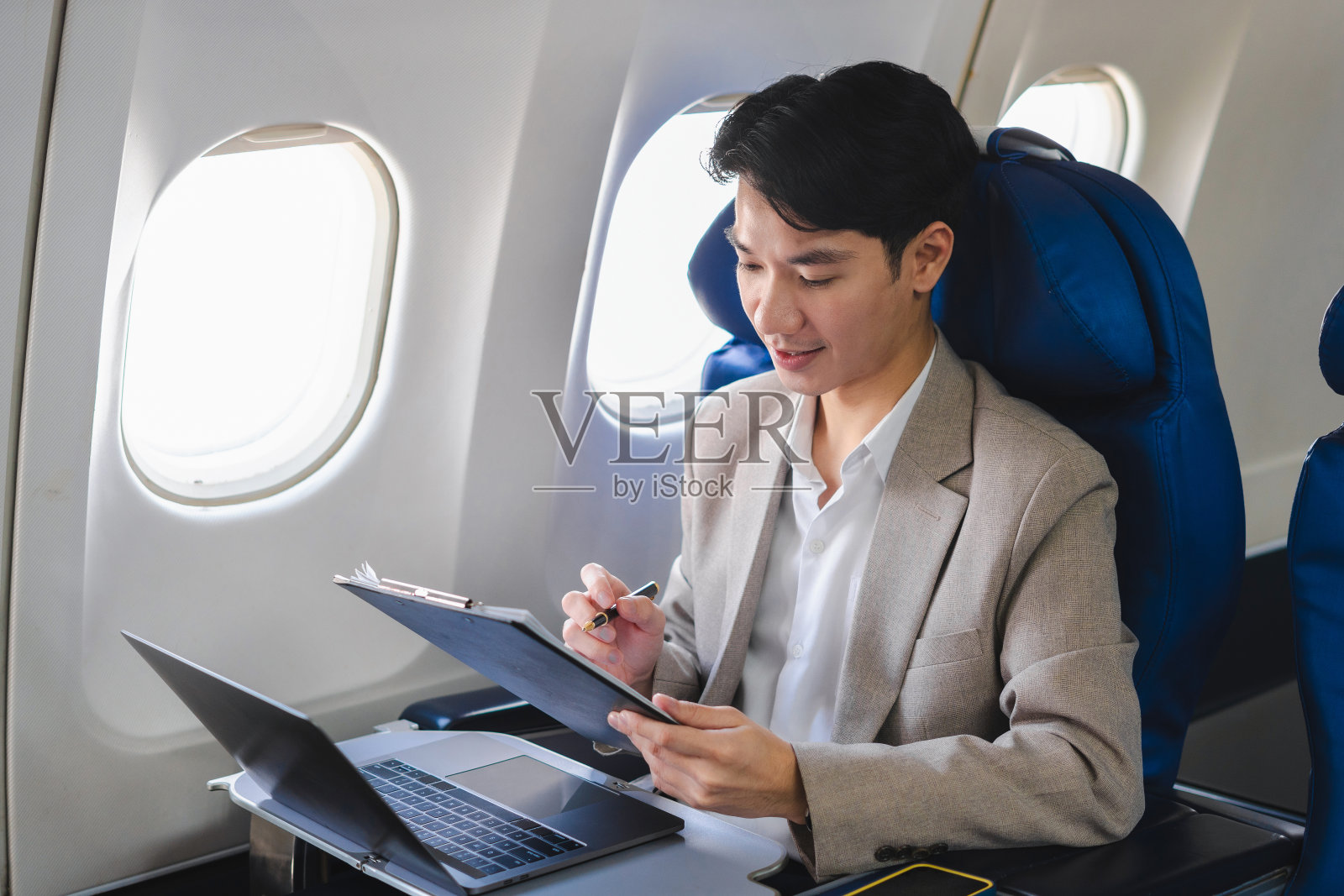 旅游和科技。快乐的年轻商人坐在飞机上用笔记本电脑和智能手机工作。照片摄影图片