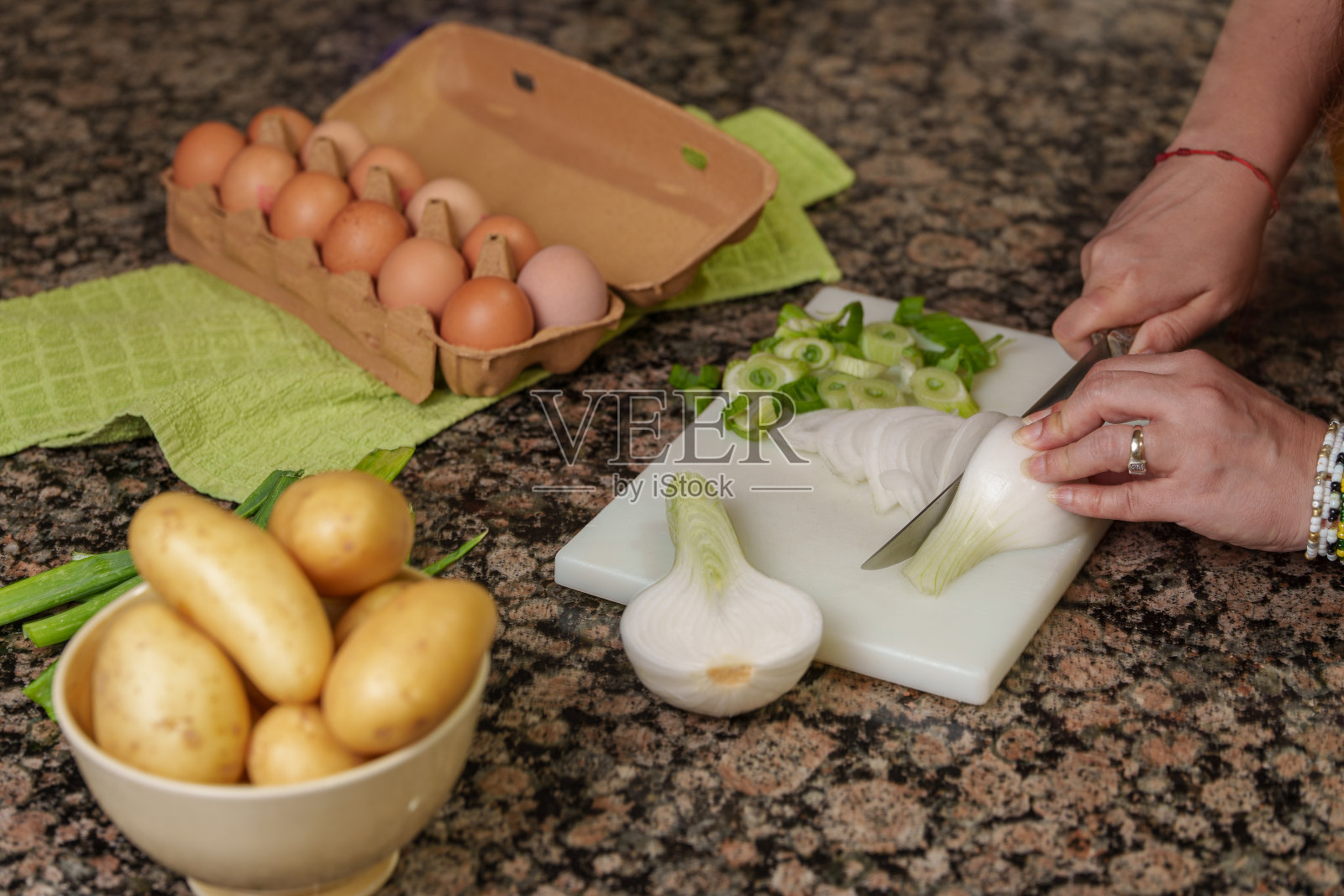 一个女人在白色的砧板上切洋葱、土豆和鸡蛋。照片摄影图片