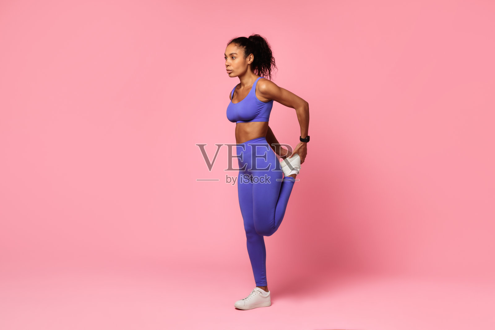 合适的非洲妇女伸展抱腿在粉红色的背景照片摄影图片