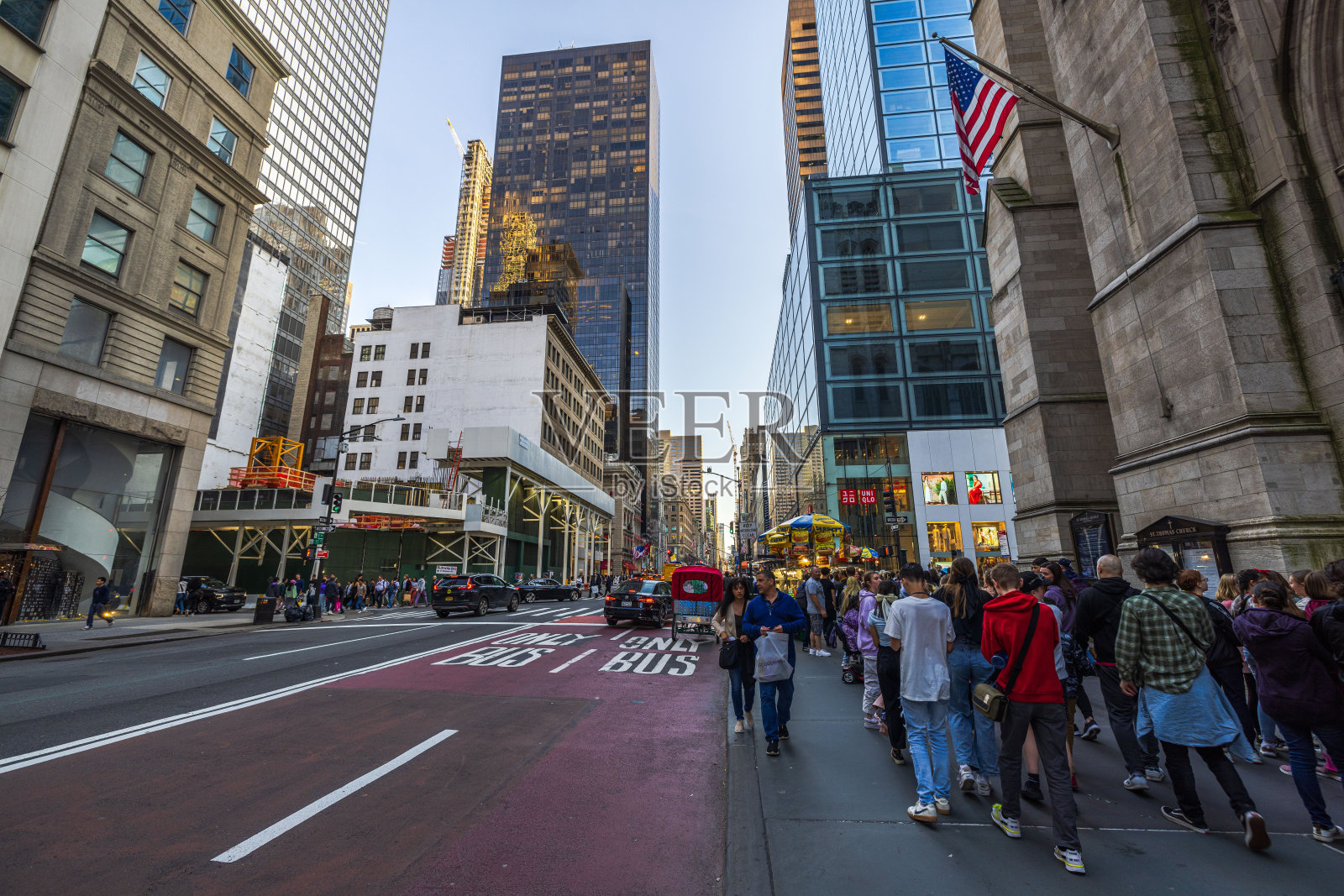 纽约曼哈顿第五大道,在高耸的摩天大楼之间的人行道上,汽车和行人熙熙攘攘。照片摄影图片