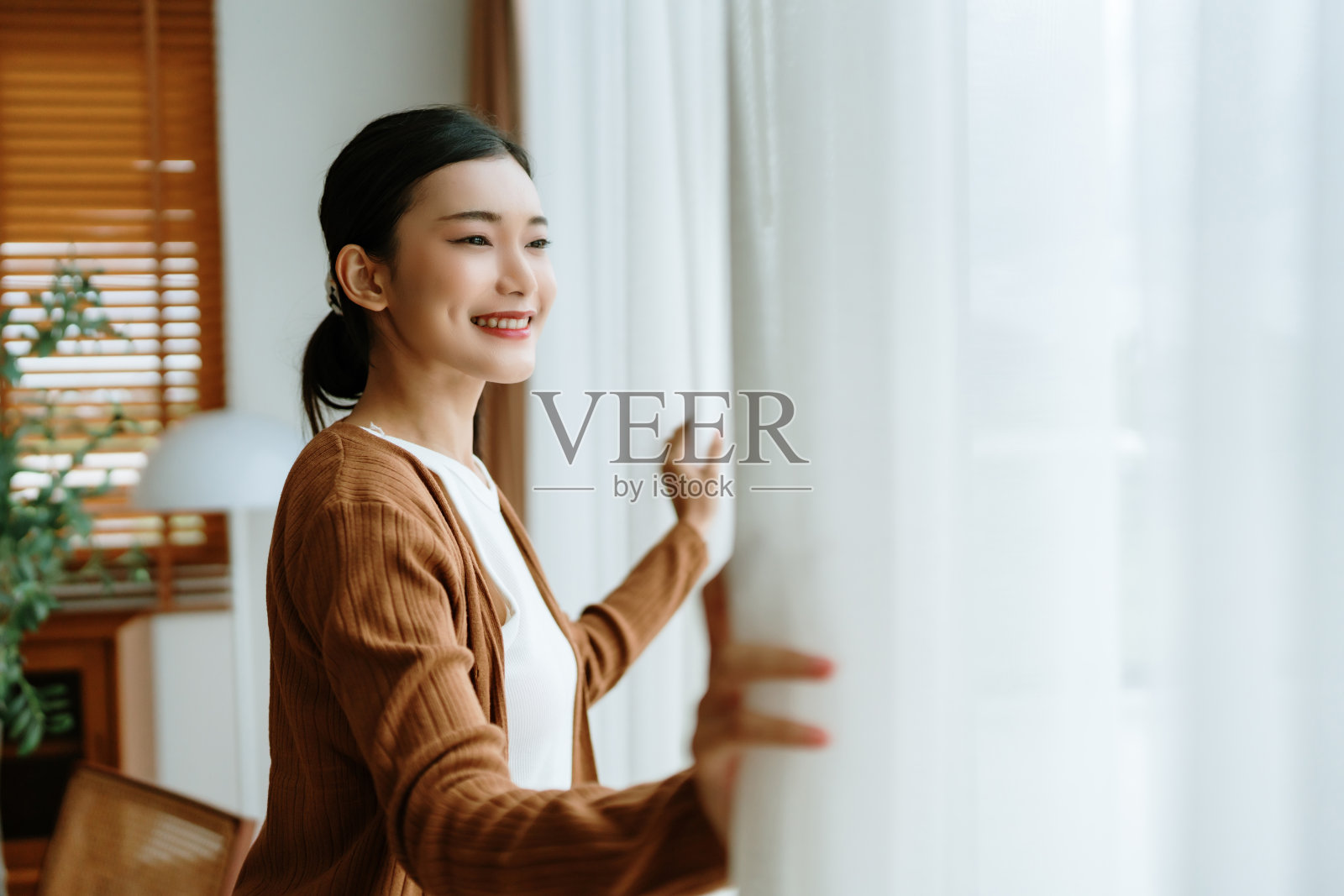 快乐的亚洲女人站在窗边，看着窗外，享受着明媚的阳光照片摄影图片