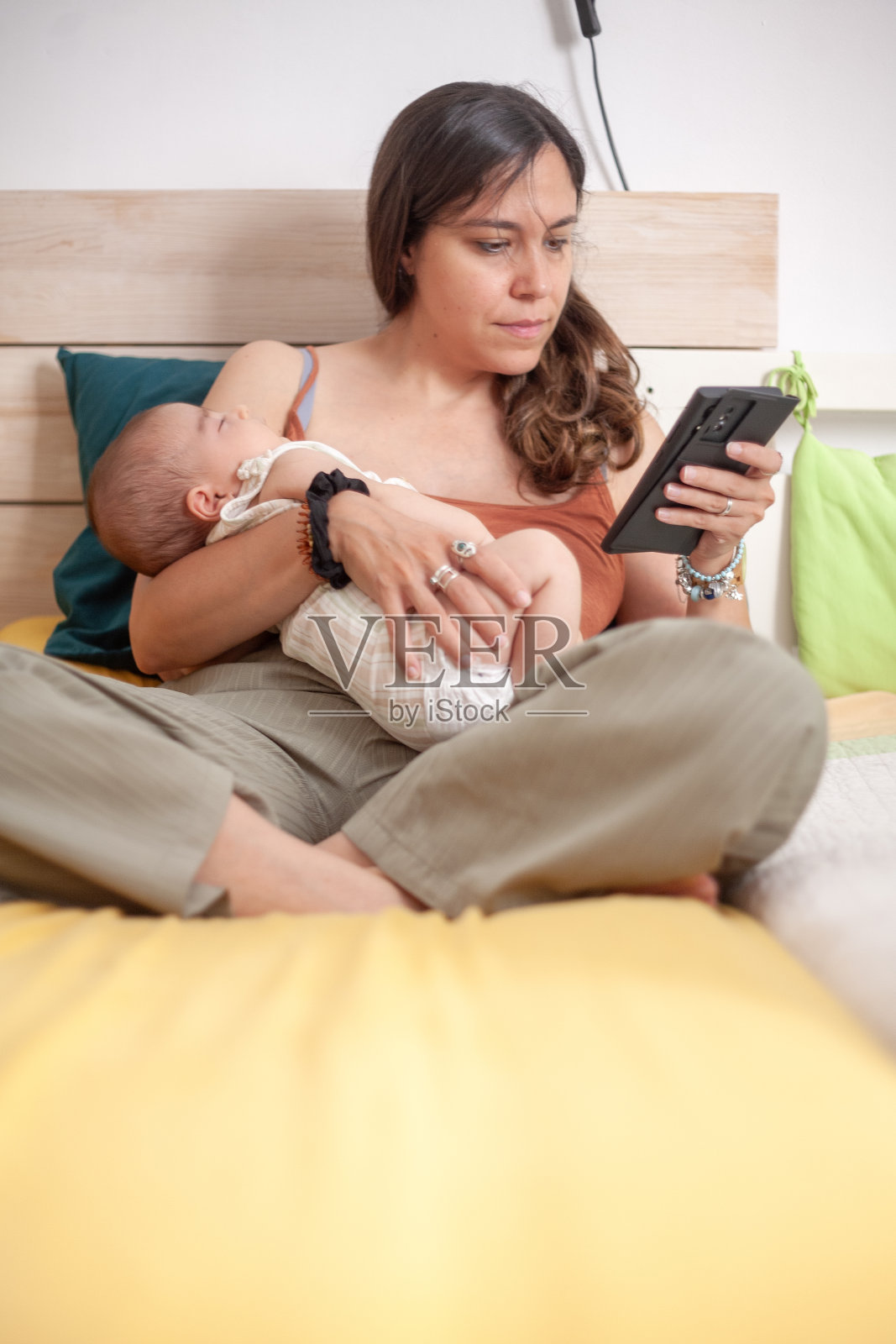 一个平静的场景，一位母亲看着手机，怀里抱着熟睡的孩子。照片摄影图片