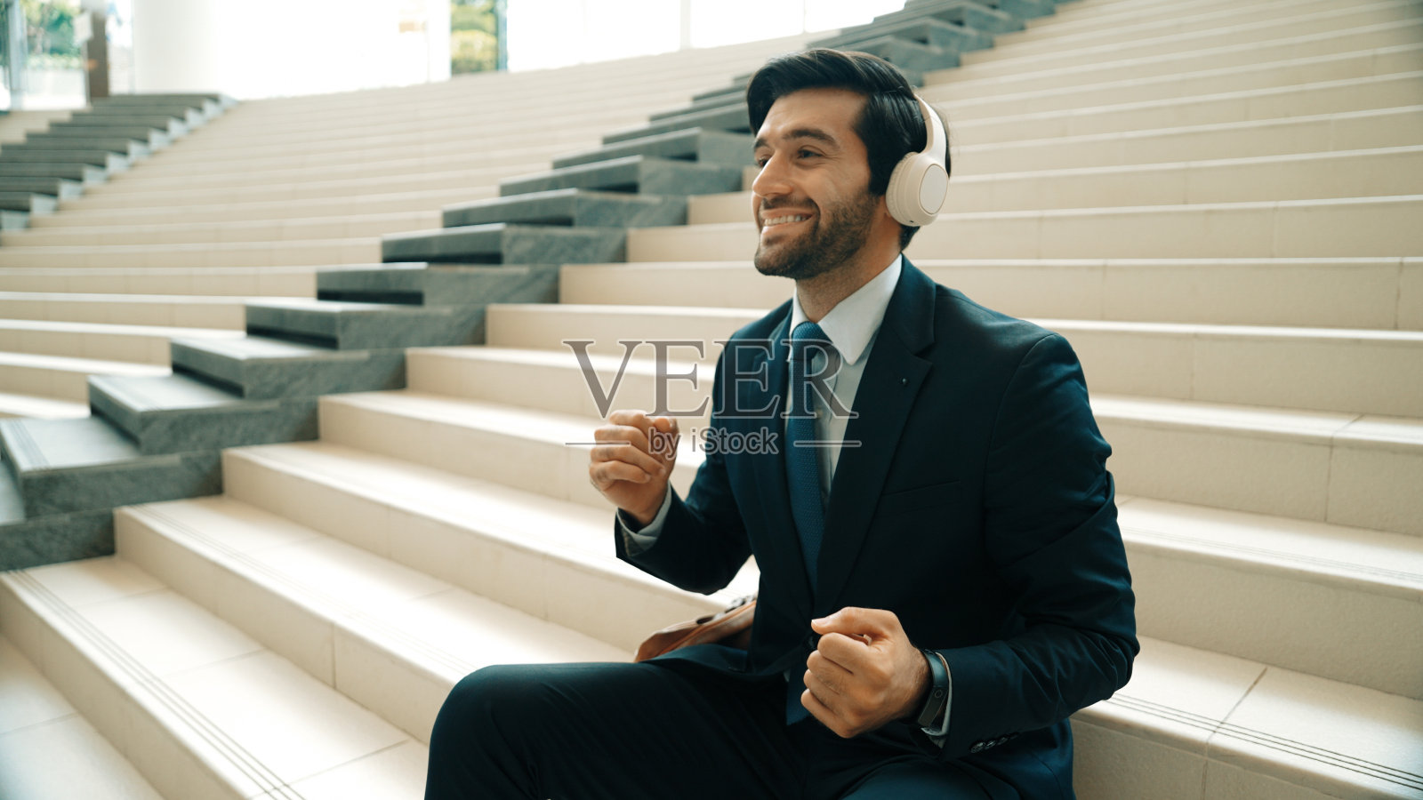 经理坐在楼梯上听耳机，享受音乐。非常高兴的。照片摄影图片