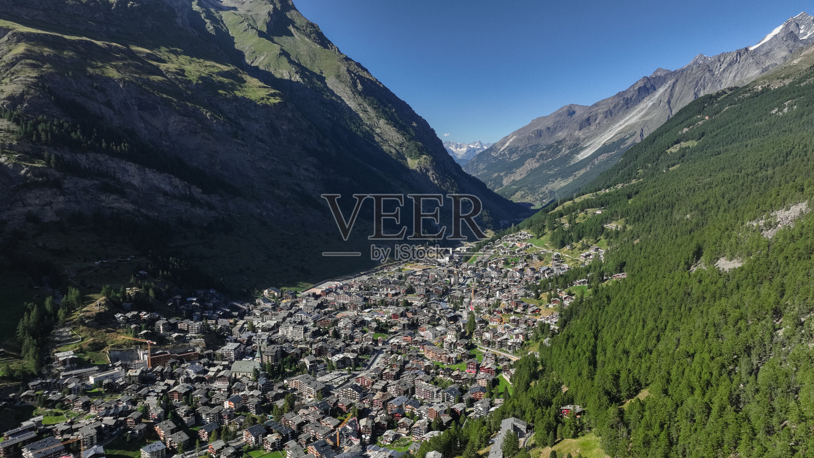 在一个晴朗的日子里，瑞士阿尔卑斯山的采尔马特鸟瞰图展示了小镇和周围的山脉照片摄影图片