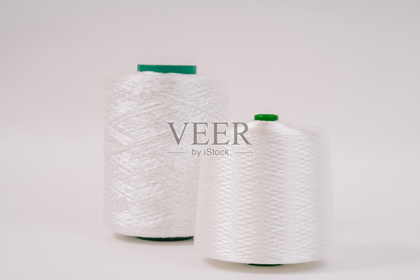 两卷白色玻璃纤维线，绿色芯，并排站在纯白色的背景，展示其光滑的质地。照片摄影图片