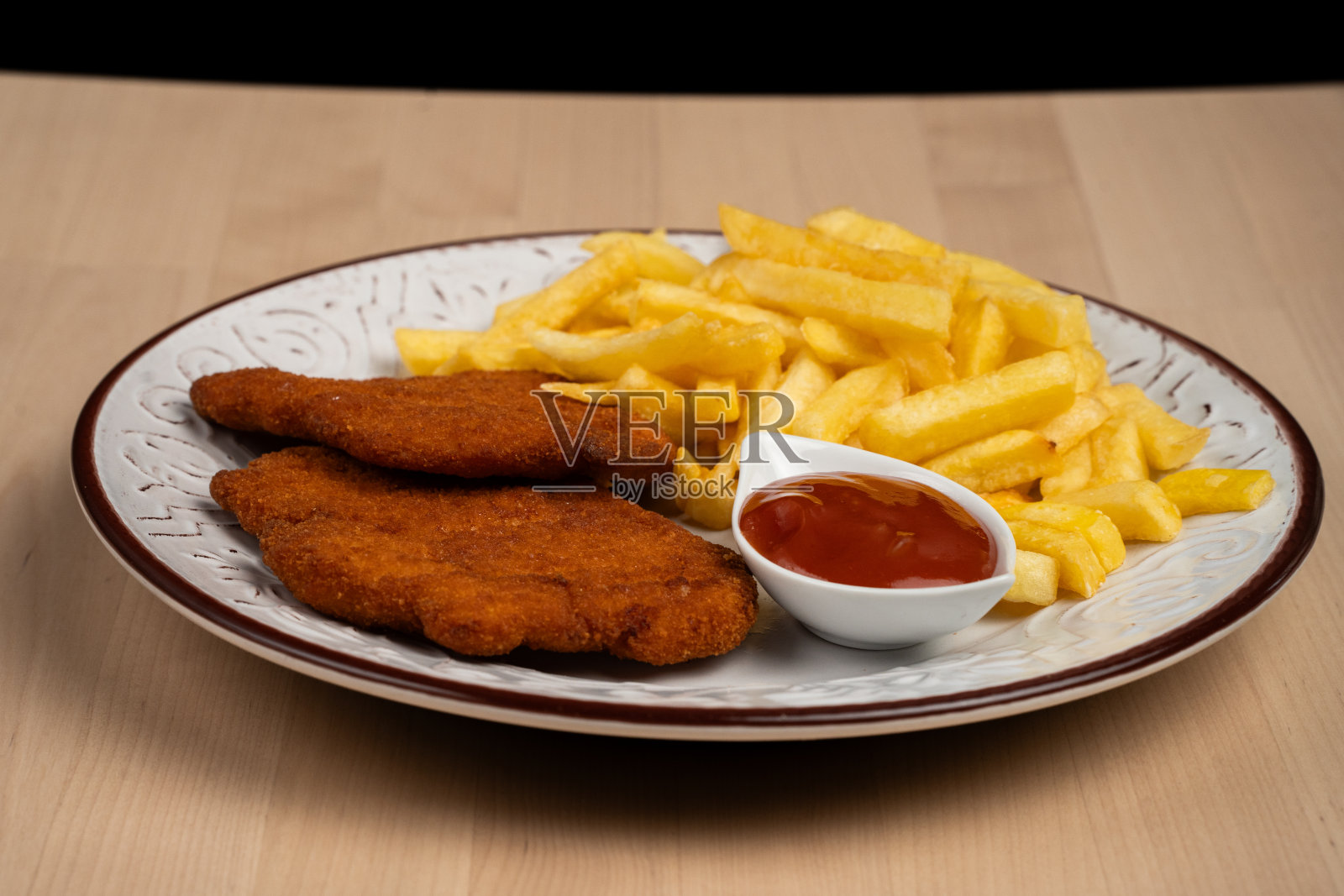 木桌上有一盘涂了面包屑的鸡排，配上金黄色的炸薯条和一盘番茄酱照片摄影图片