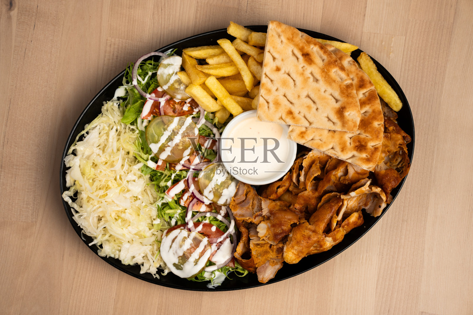 一盘美味的混合烤肉串沙拉，薯条，皮塔饼，和酱汁在一个木制的桌子上照片摄影图片