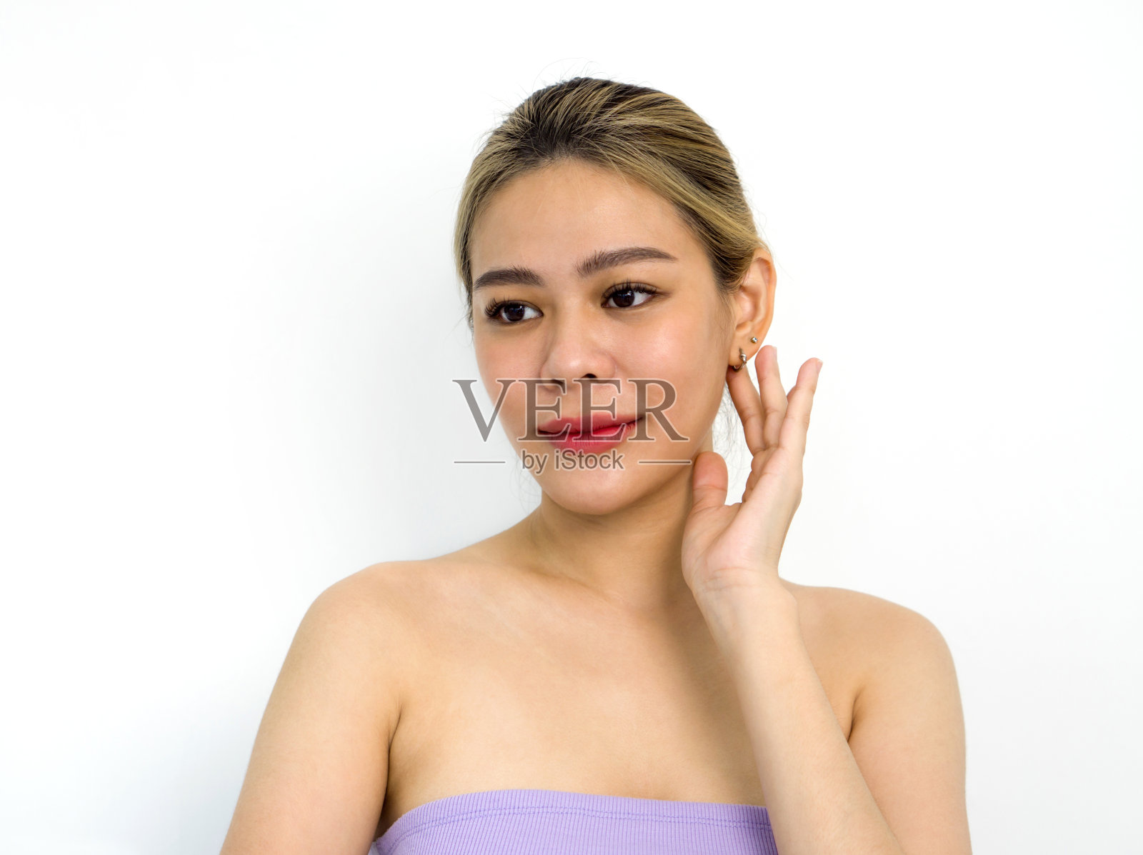 一个穿着紫色上衣的金发女人轻轻地摸着她的耳朵。肖像在白色背景与工作室照明。照片摄影图片