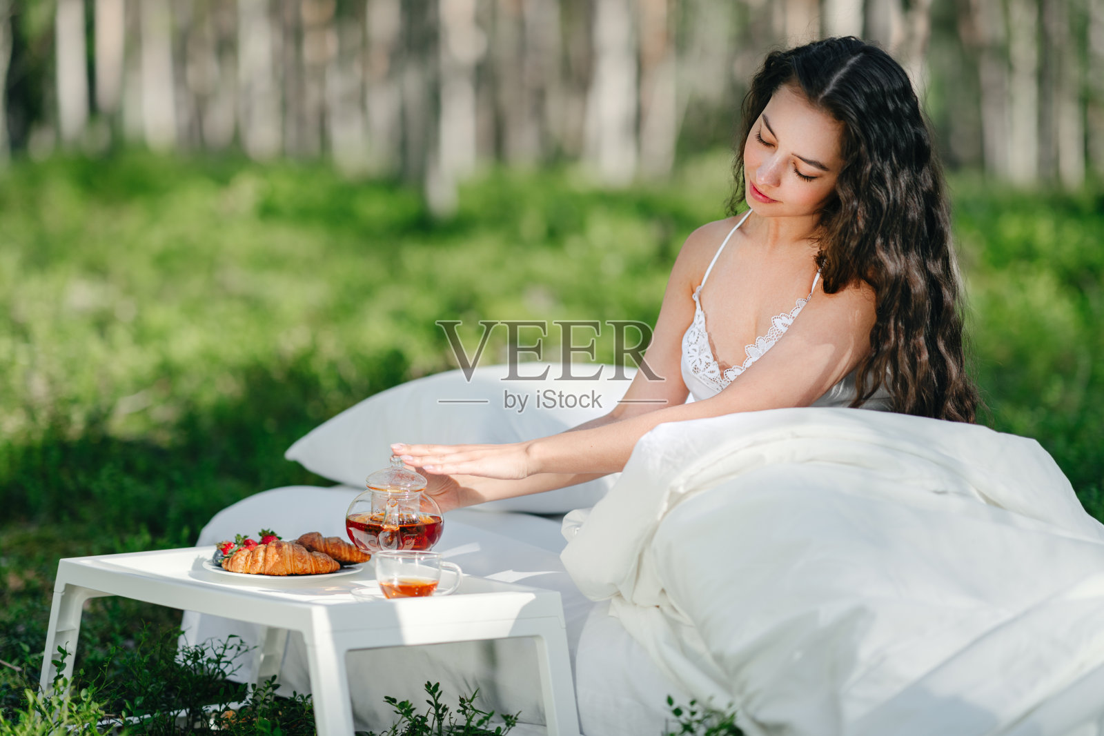 夏日森林里，一位年轻女子在床上吃早餐照片摄影图片