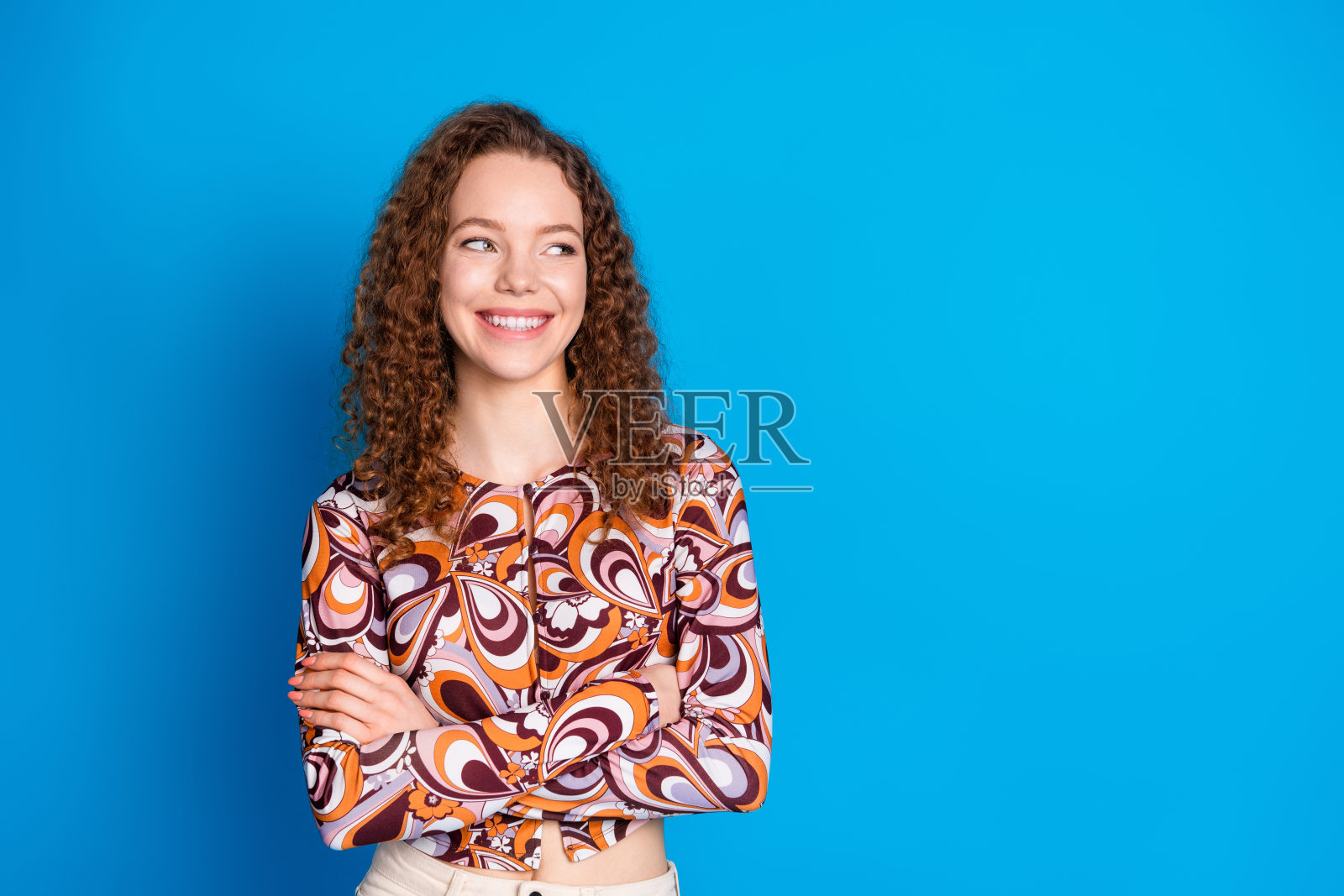 照片中可爱的年轻女士双手交叉，看起来空空荡荡，穿着时尚的彩色服装，孤立在蓝色的背景上照片摄影图片
