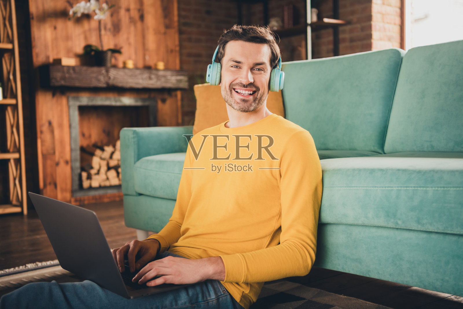 年轻人的照片肖像坐在地板上网本耳机穿着黄色的衣服花消遣宽敞的房子在室内房间照片摄影图片