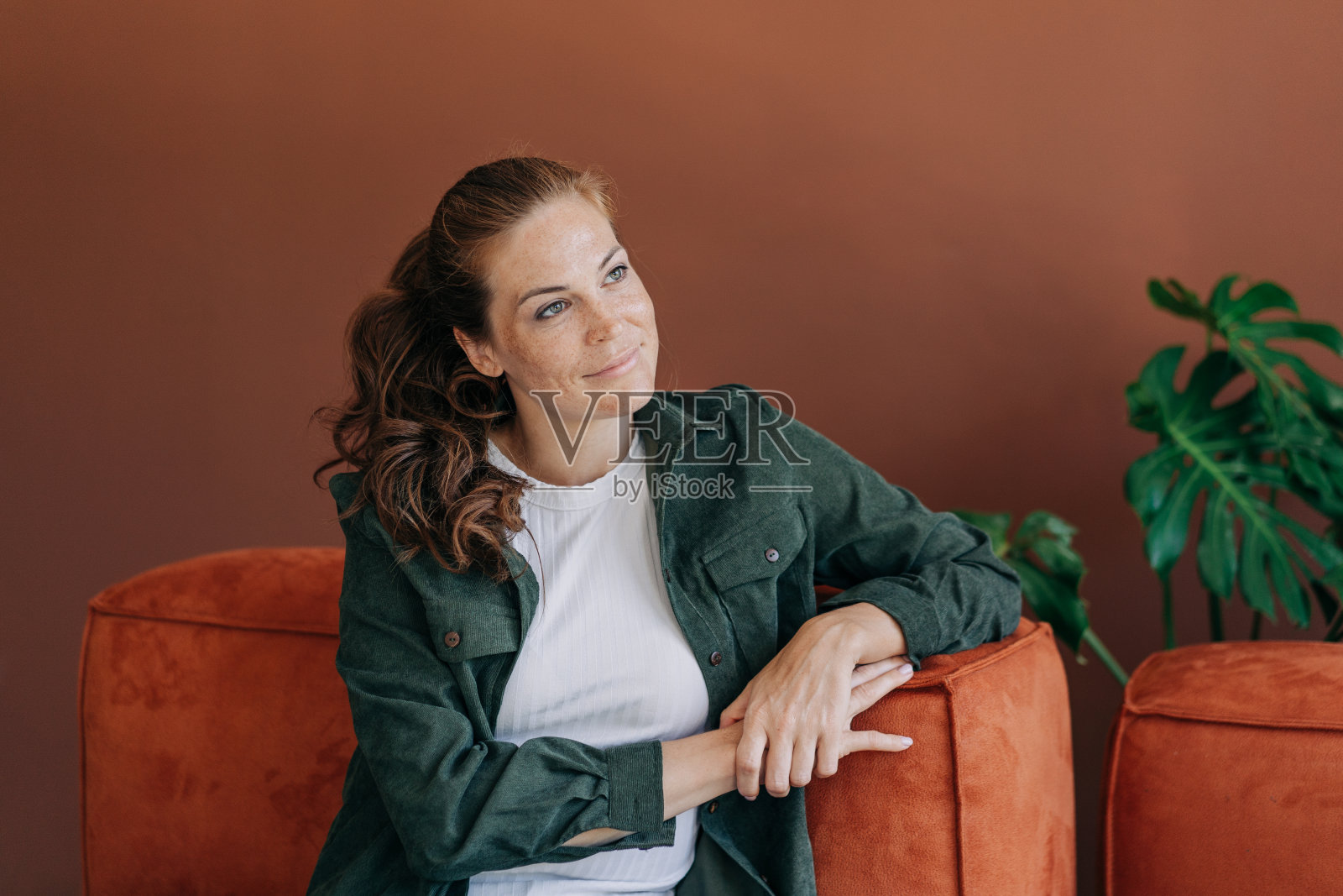 一位漂亮的年轻女子坐在沙发上若有所思地微笑着。照片摄影图片