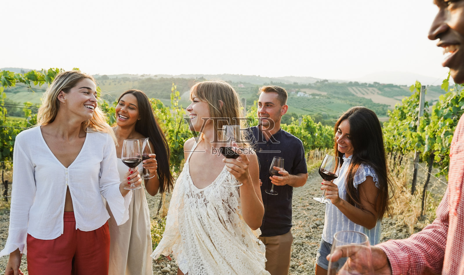 多种族的朋友在葡萄园里的夏日派对上跳舞-快乐的人们在乡村度假胜地喝红酒-旅行，庆祝和品酒活动的概念-关注中心金发女孩的脸照片摄影图片