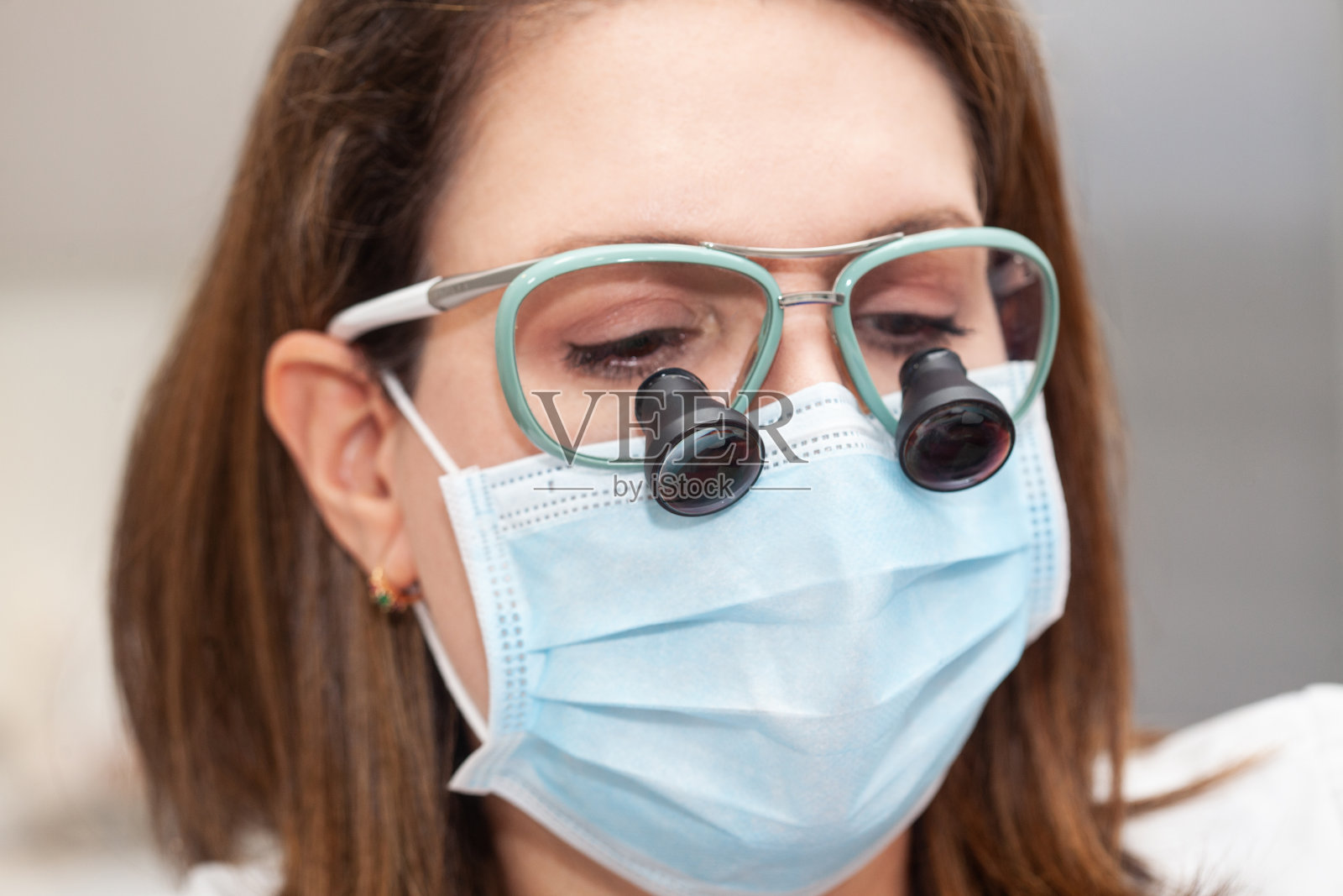 在一次小手术中，一位女皮肤科医生戴着双目镜给病人缝合时的脸部特写。照片摄影图片