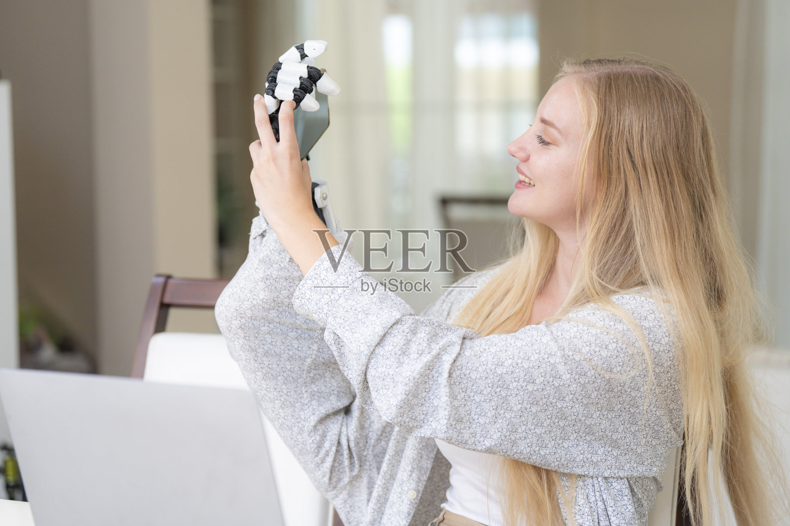 一名年轻女子正在使用附着在她身体上的机械假肢手在桌子上工作。她正在做电脑文件和通讯工作。一位女士试图控制家中的智能手臂。照片摄影图片