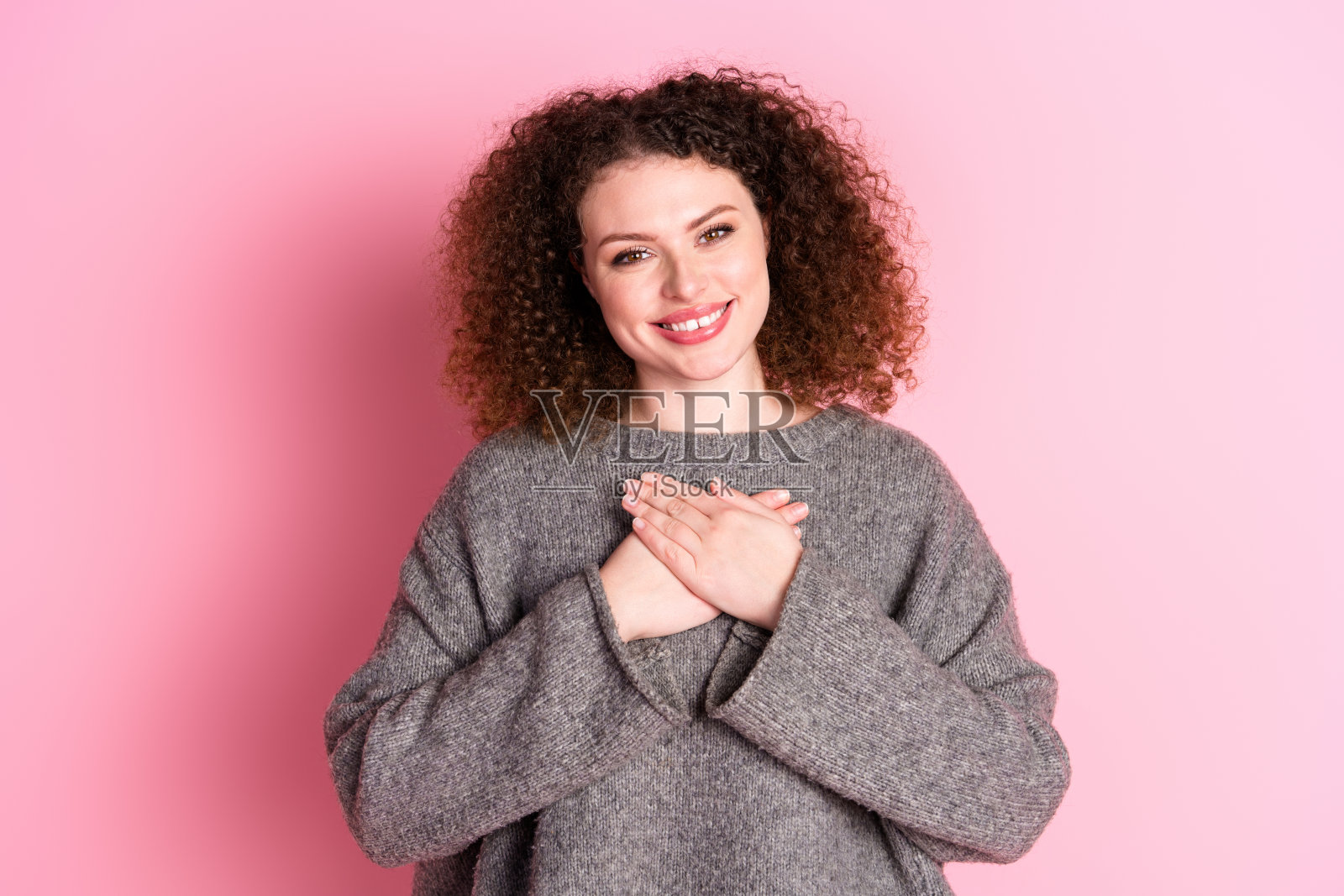 可爱的年轻女士的照片肖像触摸胸部感激穿着时尚的灰色服装孤立在粉红色的背景照片摄影图片