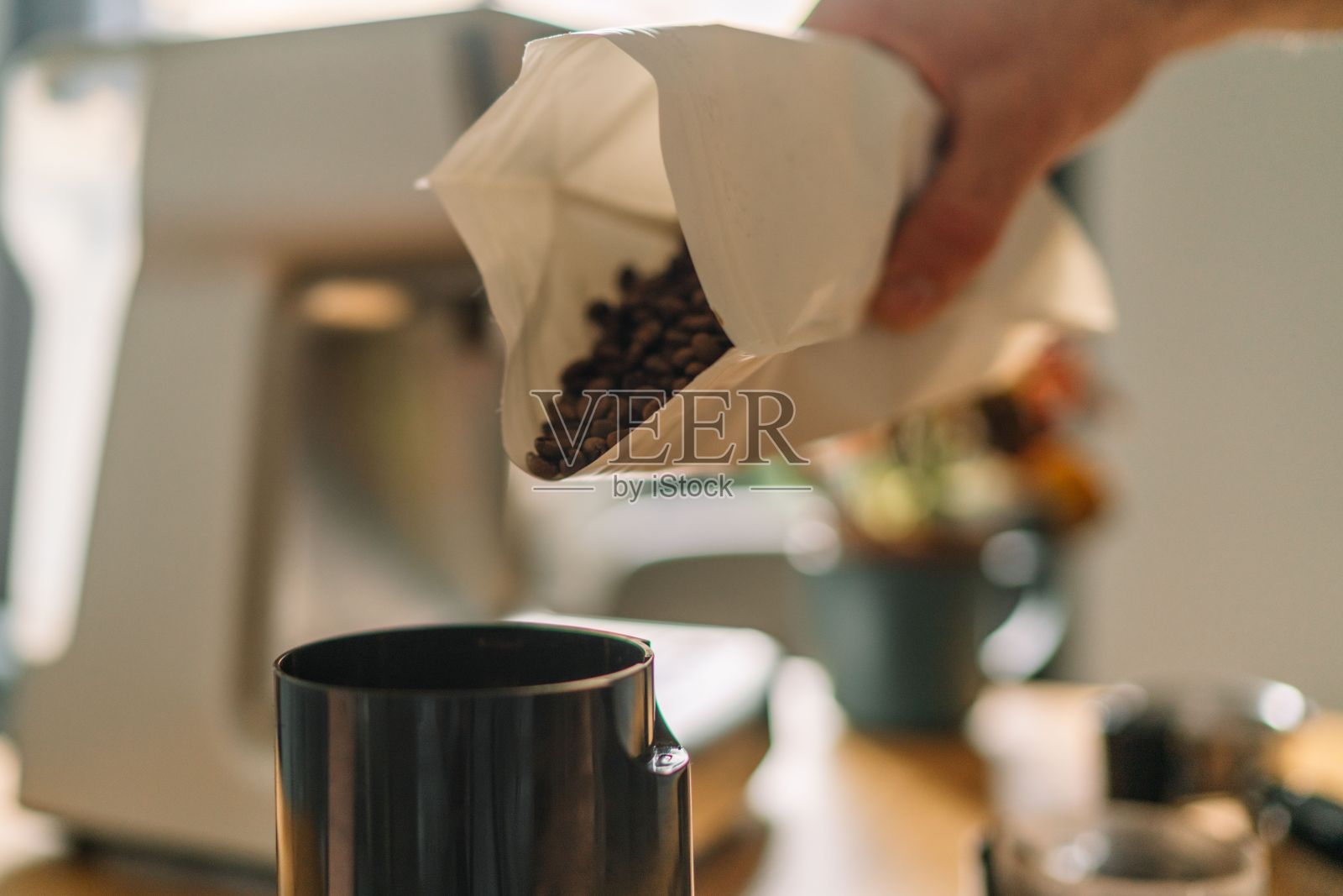 在舒适的厨房里，一只手把咖啡豆从袋子里倒进咖啡研磨机的特写照片摄影图片