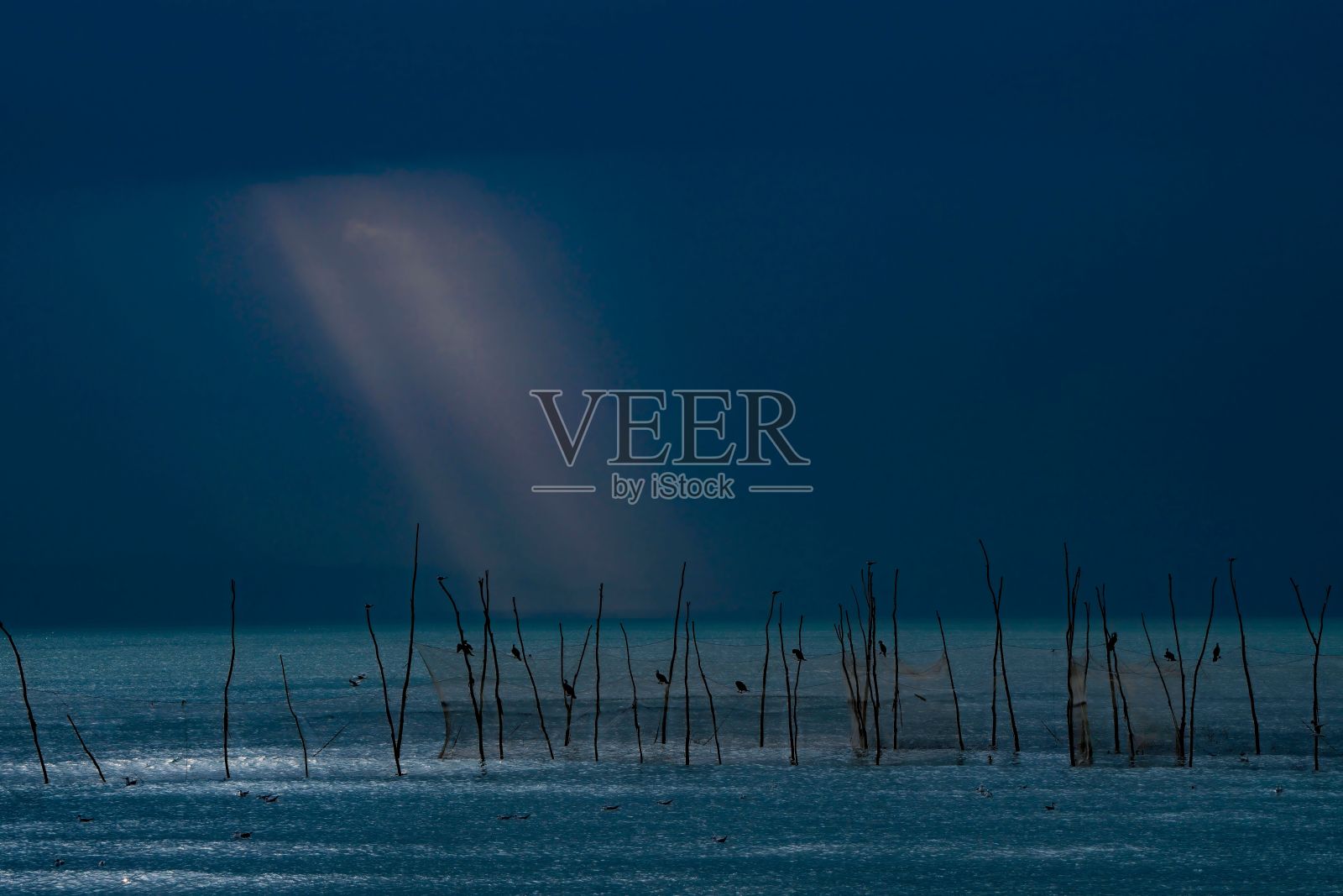 宁静的海景，阳光透过乌云和水中的木杆照片摄影图片