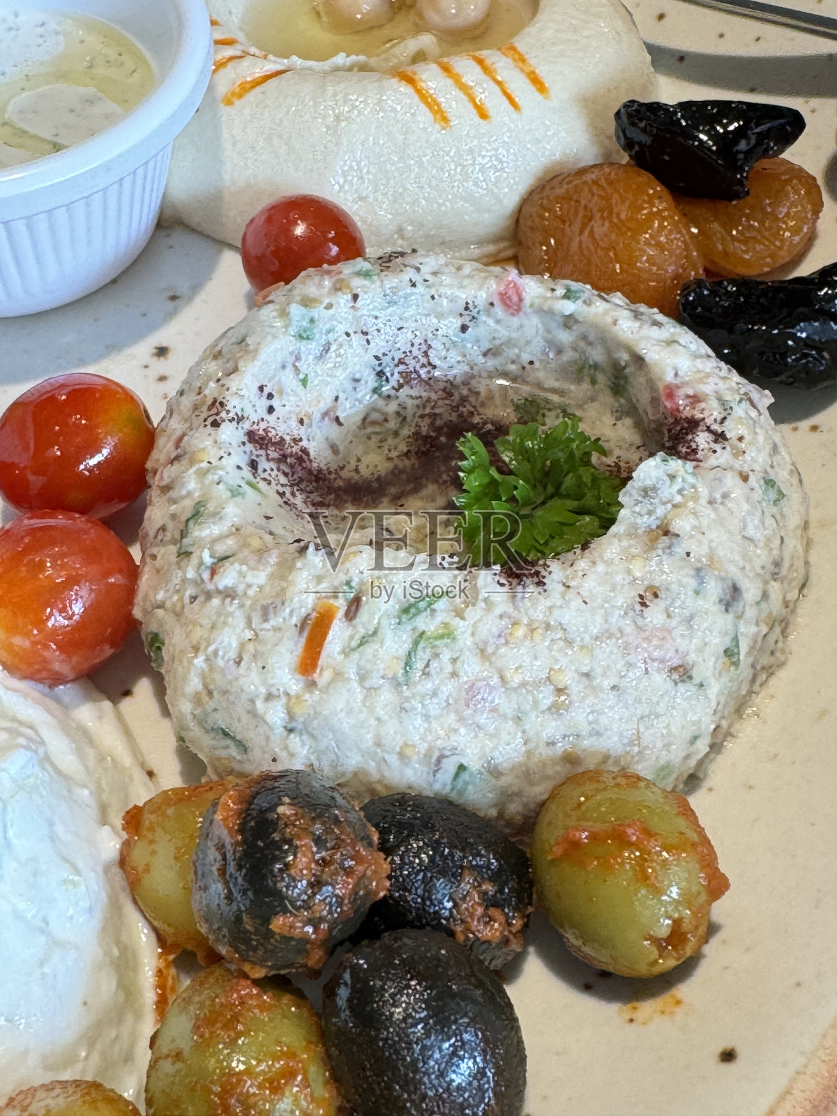 黎巴嫩meze的特写图片，开胃菜自助餐拼盘，有Baba ghanoush(茄子蘸酱)，鹰嘴豆蘸酱，圣女果，枣，杏，黑橄榄和绿橄榄，希腊酸奶，蘸酱的杯子，前景的高度聚焦照片摄影图片