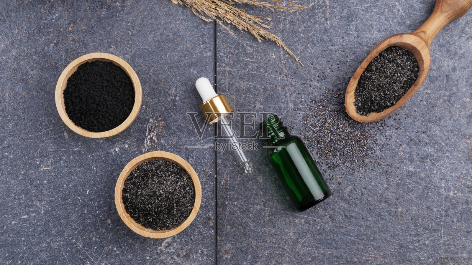 黑色孜然油瓶与新鲜的黑色孜然粉末在一个灰色的表面。照片摄影图片