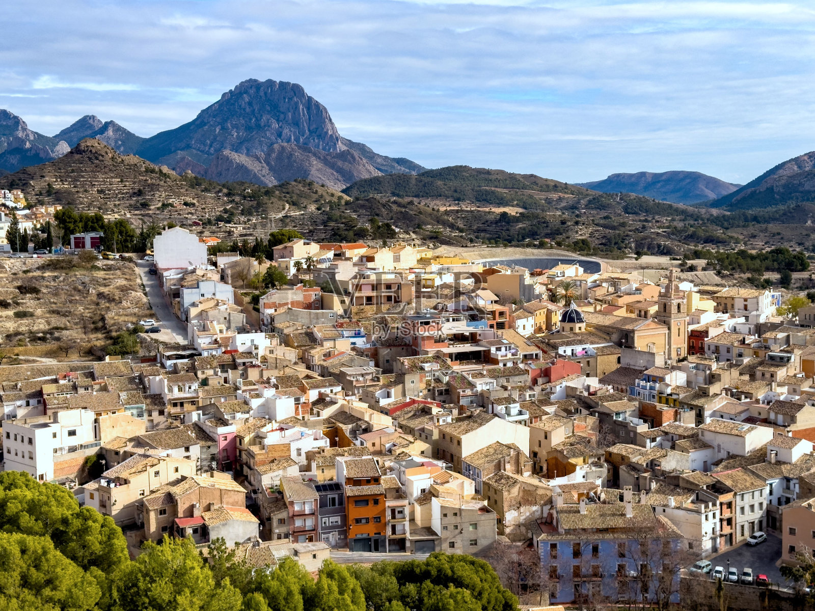 在一个阳光明媚的日子里，Relleu镇的前景是树木，背景是山照片摄影图片