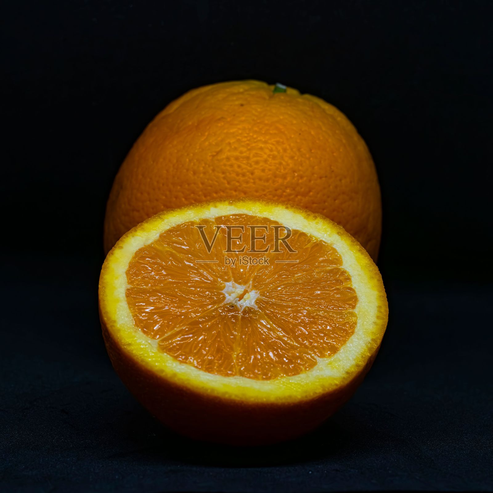 一个新鲜橙子的特写镜头，在黑暗的背景下切开一半。照片摄影图片